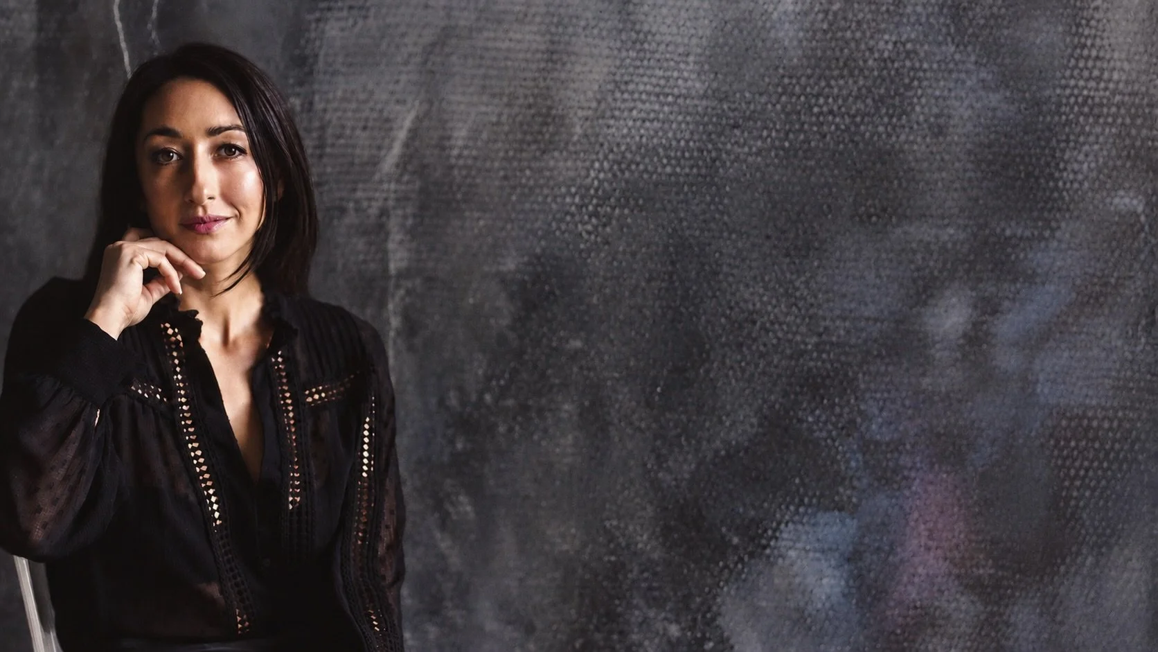 Eloise Parker wearing a black blouse with long dark hair sitting against a textured metallic wall.