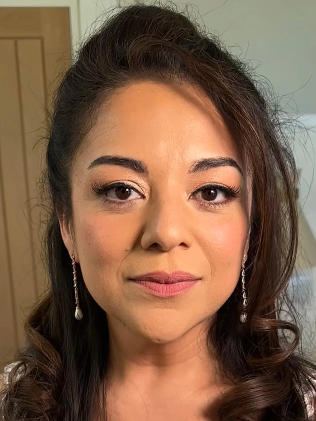 A woman with styled dark brown hair, makeup, and dangling pearl earrings.