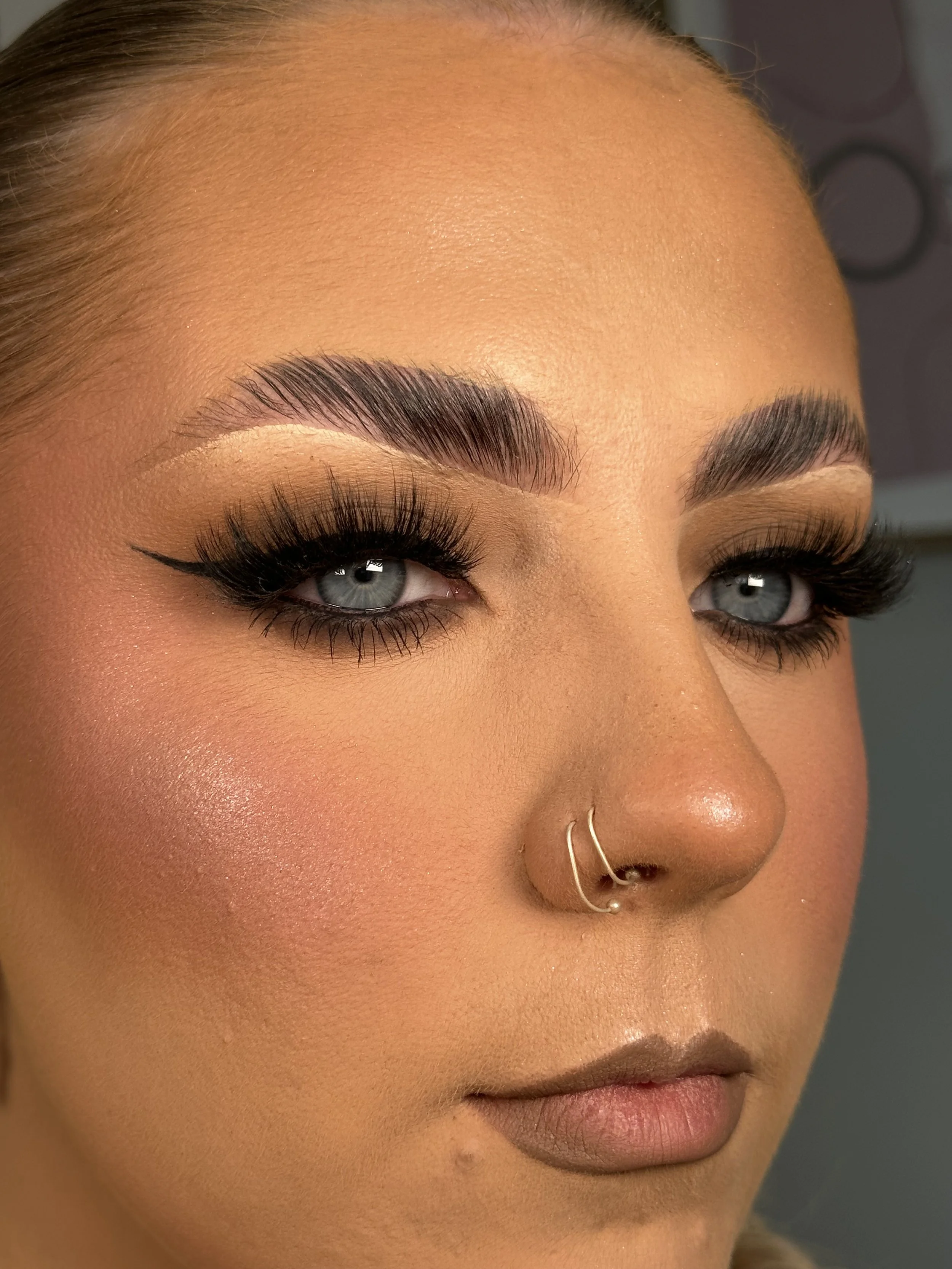 Close-up of a woman's face focusing on her eyes, eyebrows, nose, and lips, with makeup and jewelry visible.