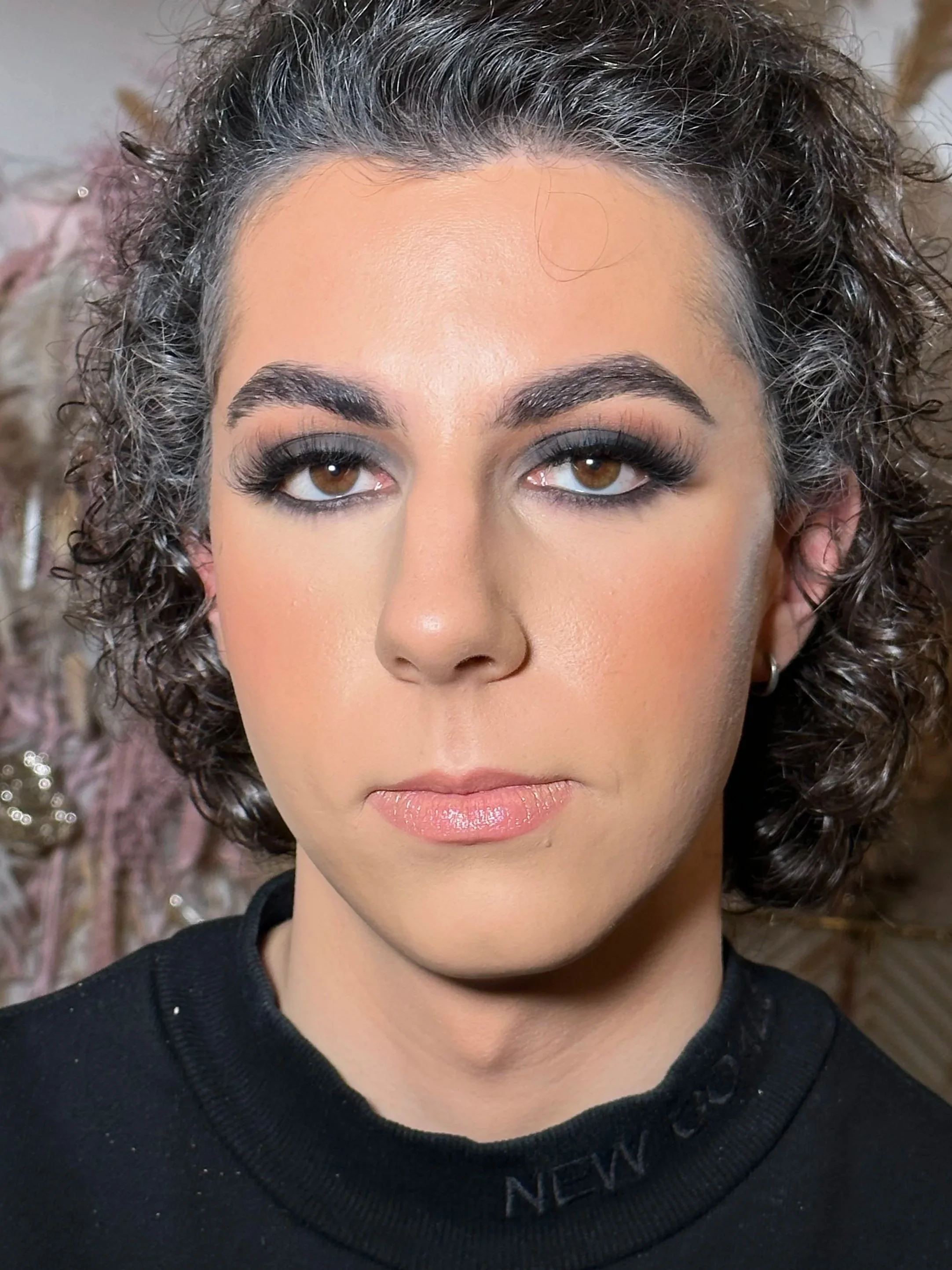 Close-up of a woman's face showing her eyes and makeup, with curly hair and a dark top.