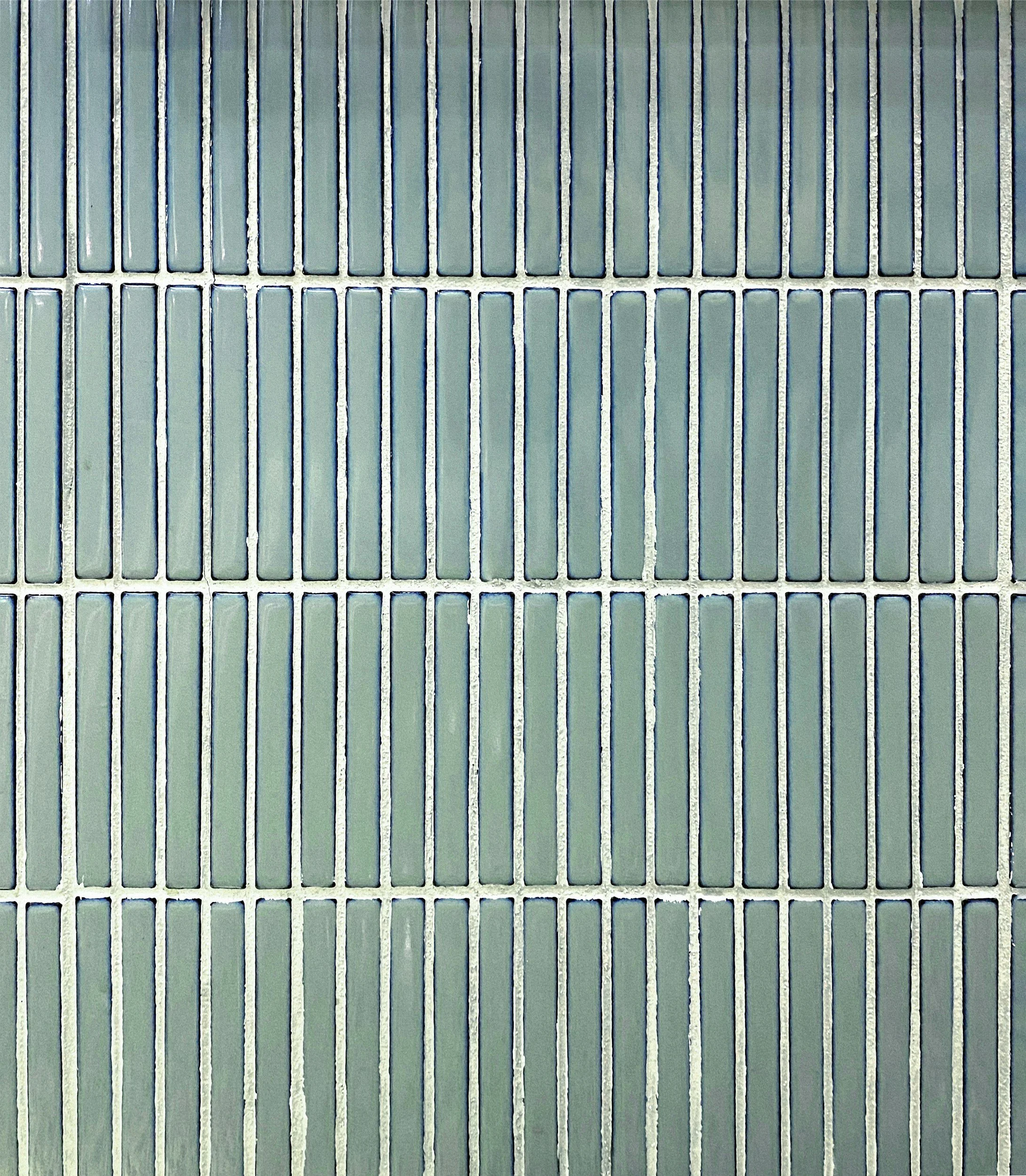 Close-up view of a square tiled surface with gray grout lines. The tiles are rectangular and light greenish-gray.