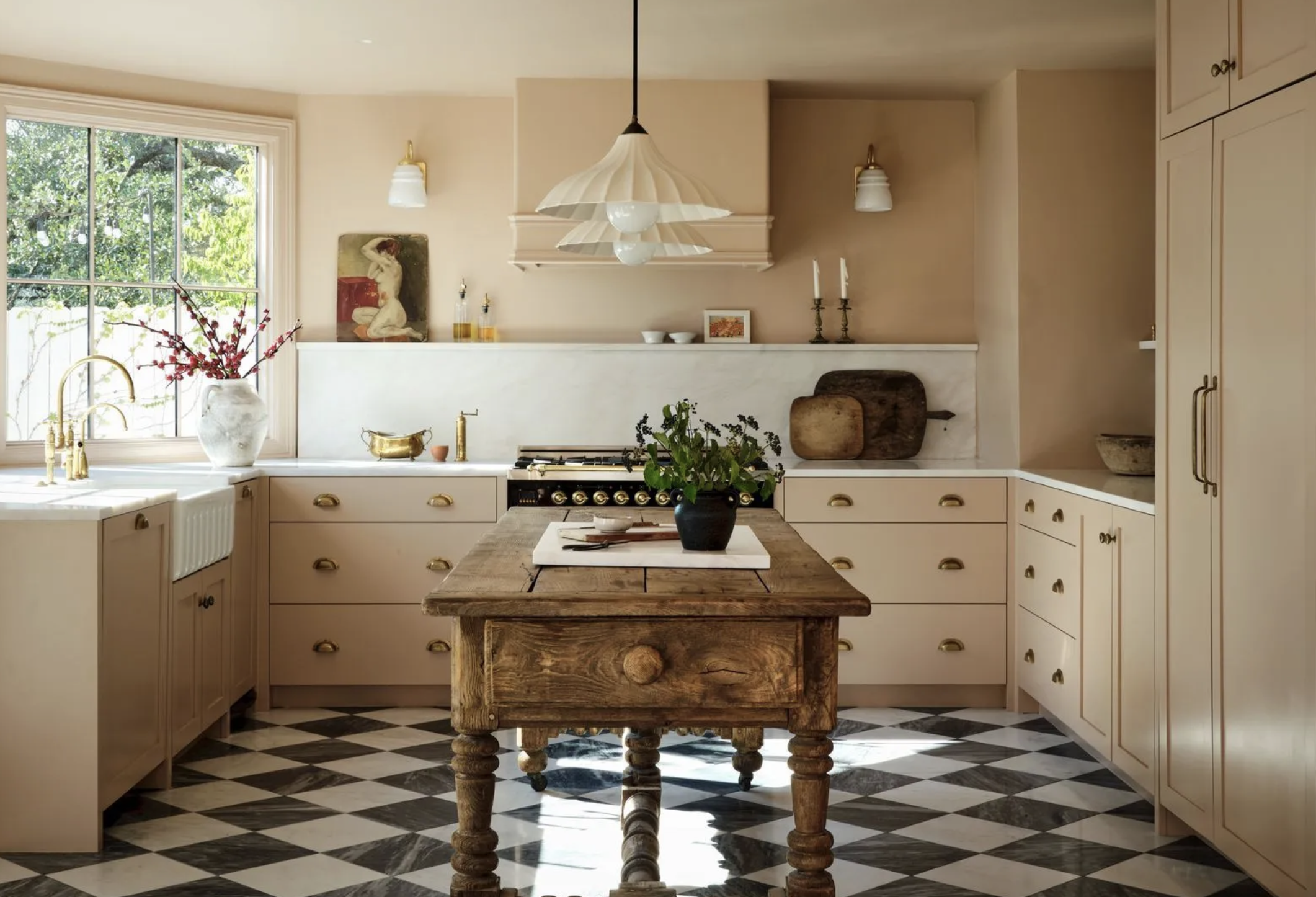 Bright kitchen with beige cabinets, black and white checkered floor, a large window, a wooden table, and shelves with decorative items.