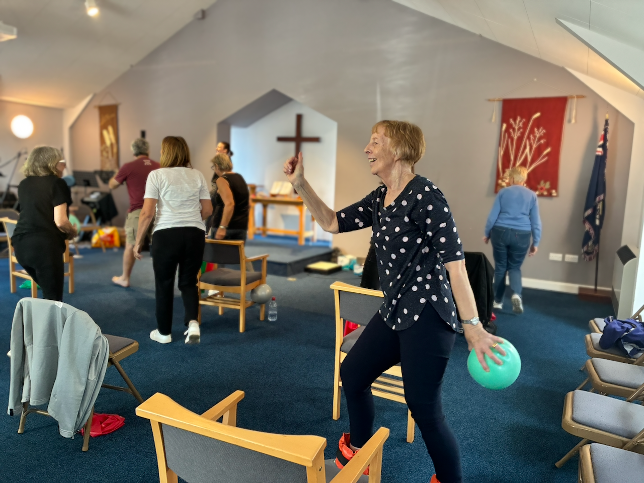 A group of women participating in a church exercise class, with one woman laughing and holding a green exercise ball.
