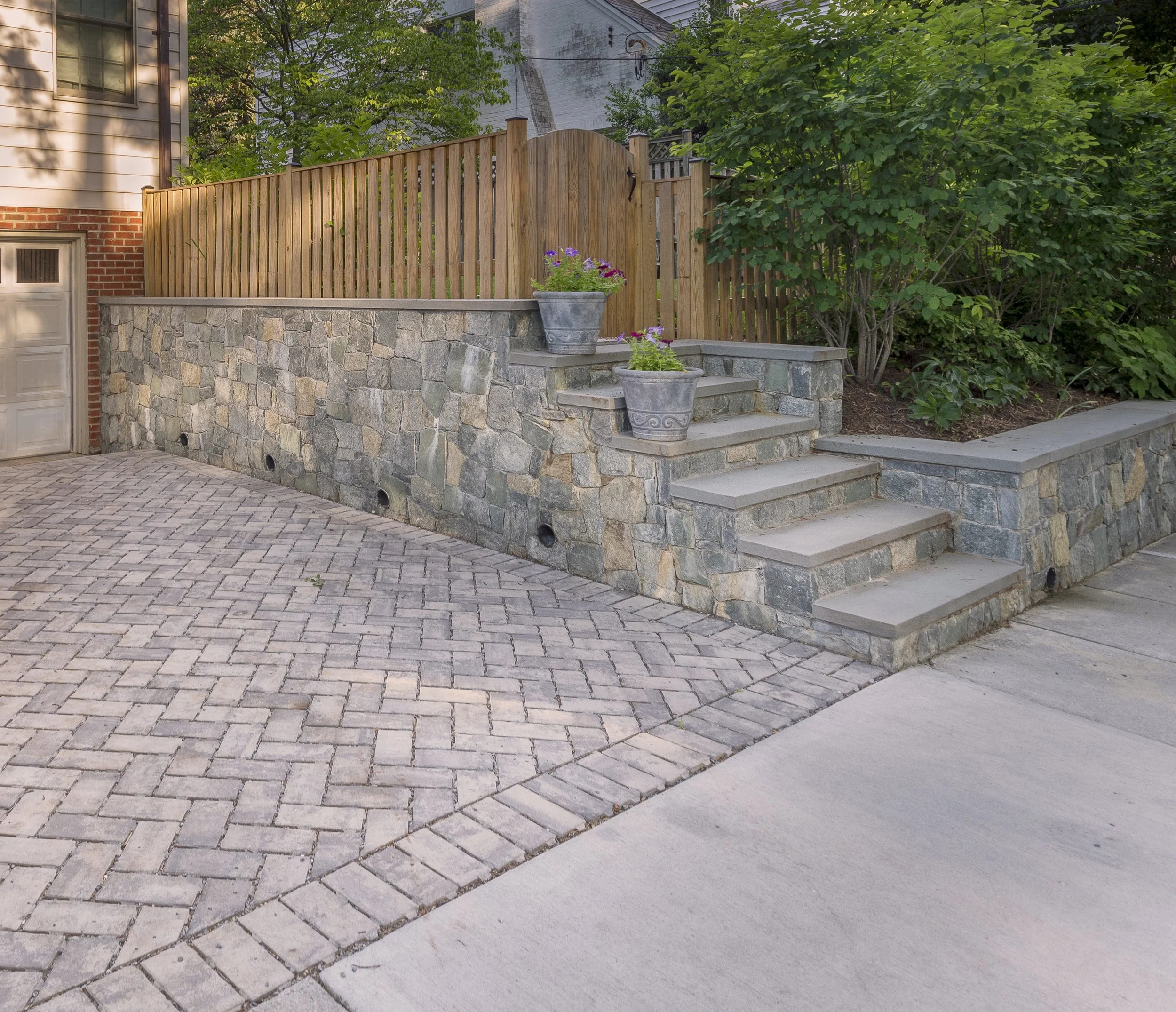 Techo Bloc Pavers for a new permeable paving driveway design. New natural stone retaining walls and custom cedar fencing create privacy in the garden. 
