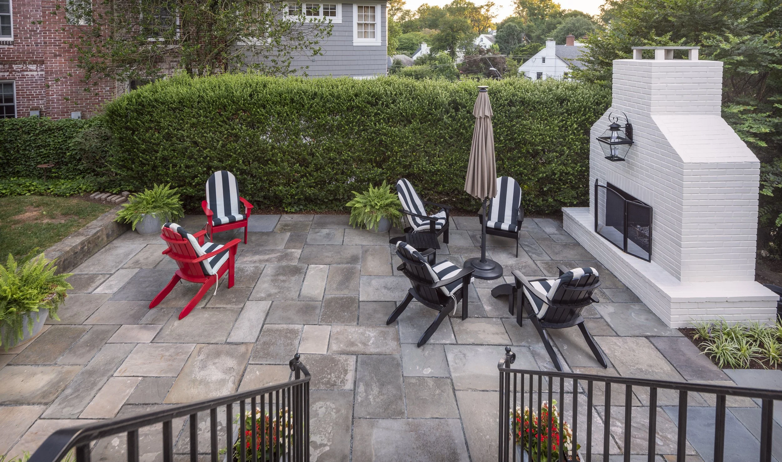 A small courtyard is transformed by a simple landscape design featuring an outdoor fireplace, simple privacy plantings, and precision laid natural stone paving. NW DC