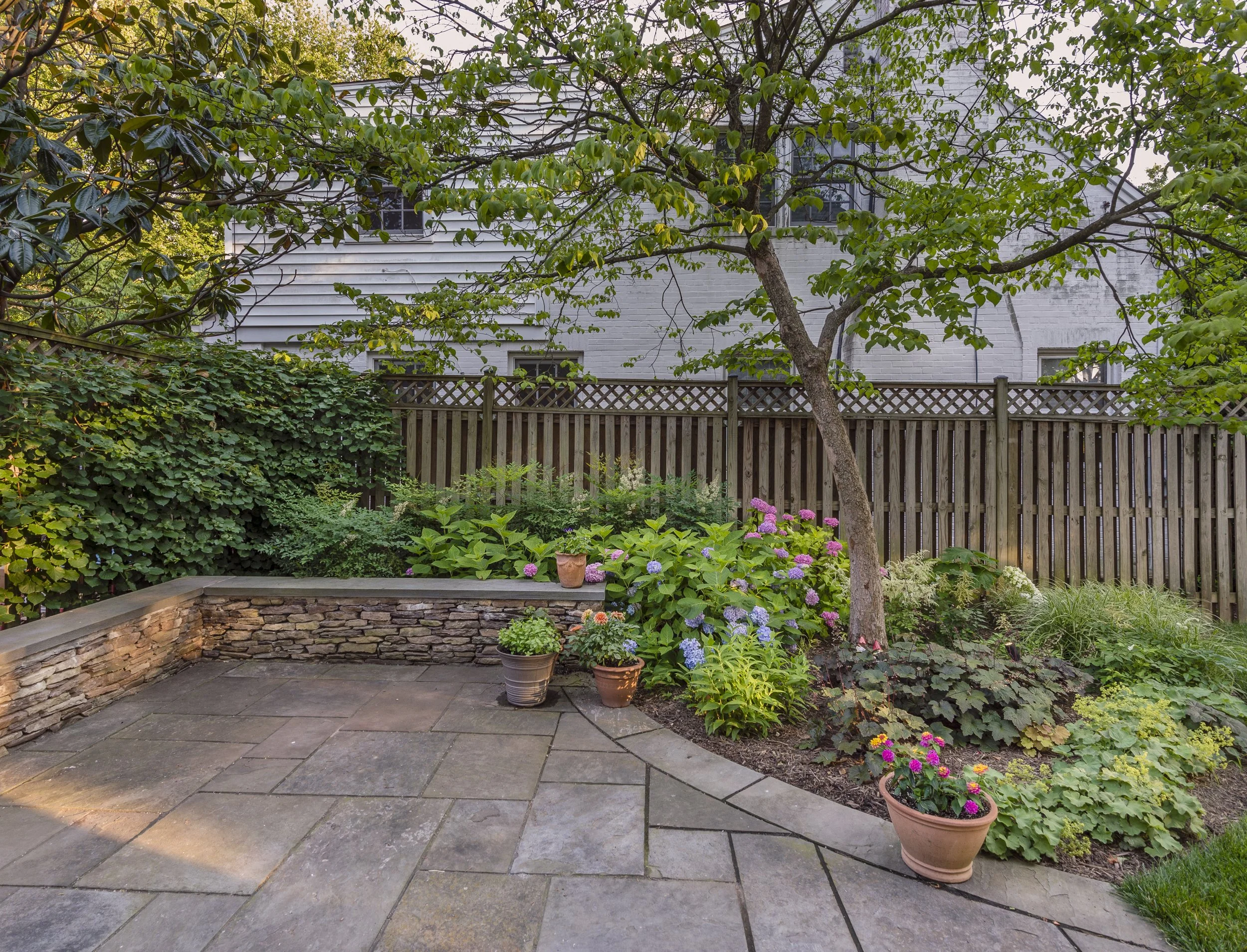 Colorful plantings enhance a mature Dogwood tree. Natural stone seat walls increase space for outdoor entertaining
