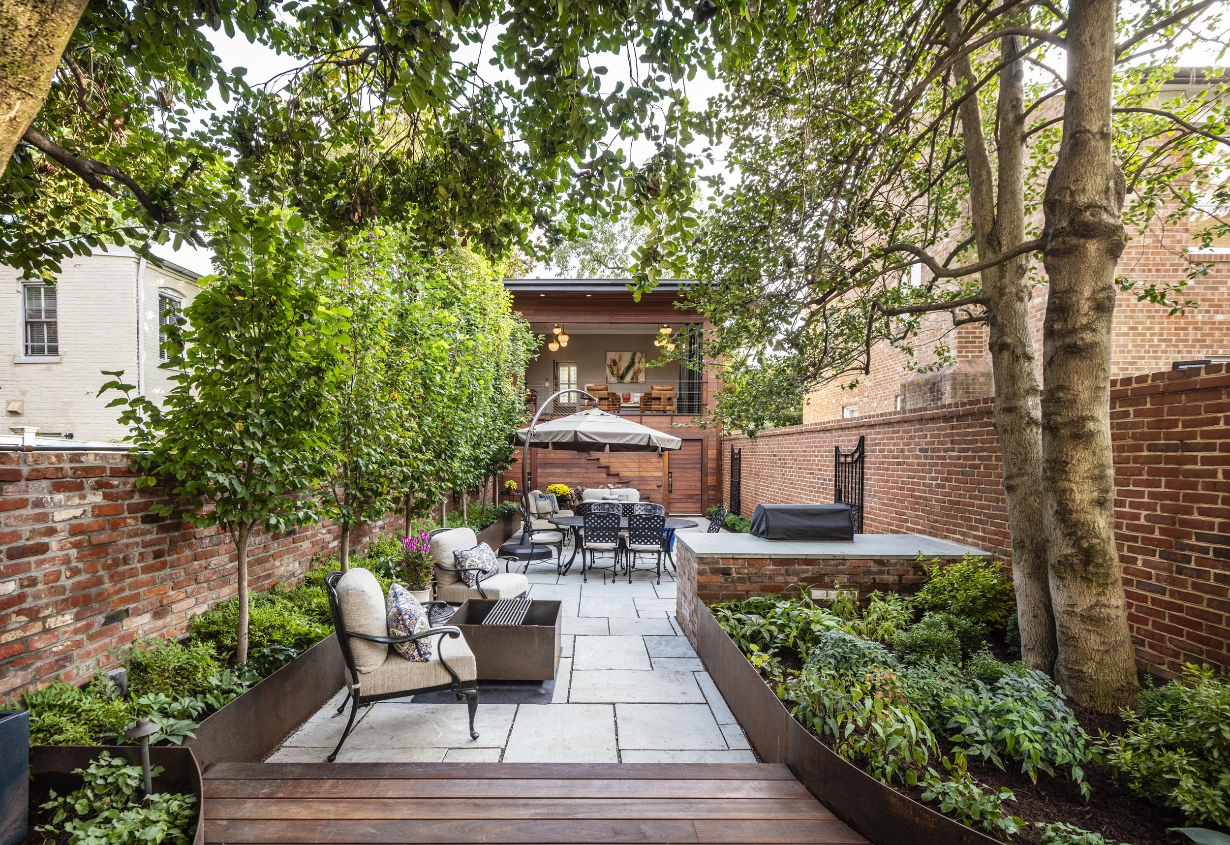 Small space garden design with an Ipe wood deck leads down to beautiful natural stone paving that compliments the historic brick walls. Built-in cor-ten steel panels create planters for screening plantings to increase privacy. 