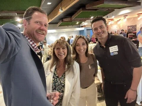 Four people smiling and taking a selfie at a social event in a restaurant or cafe.