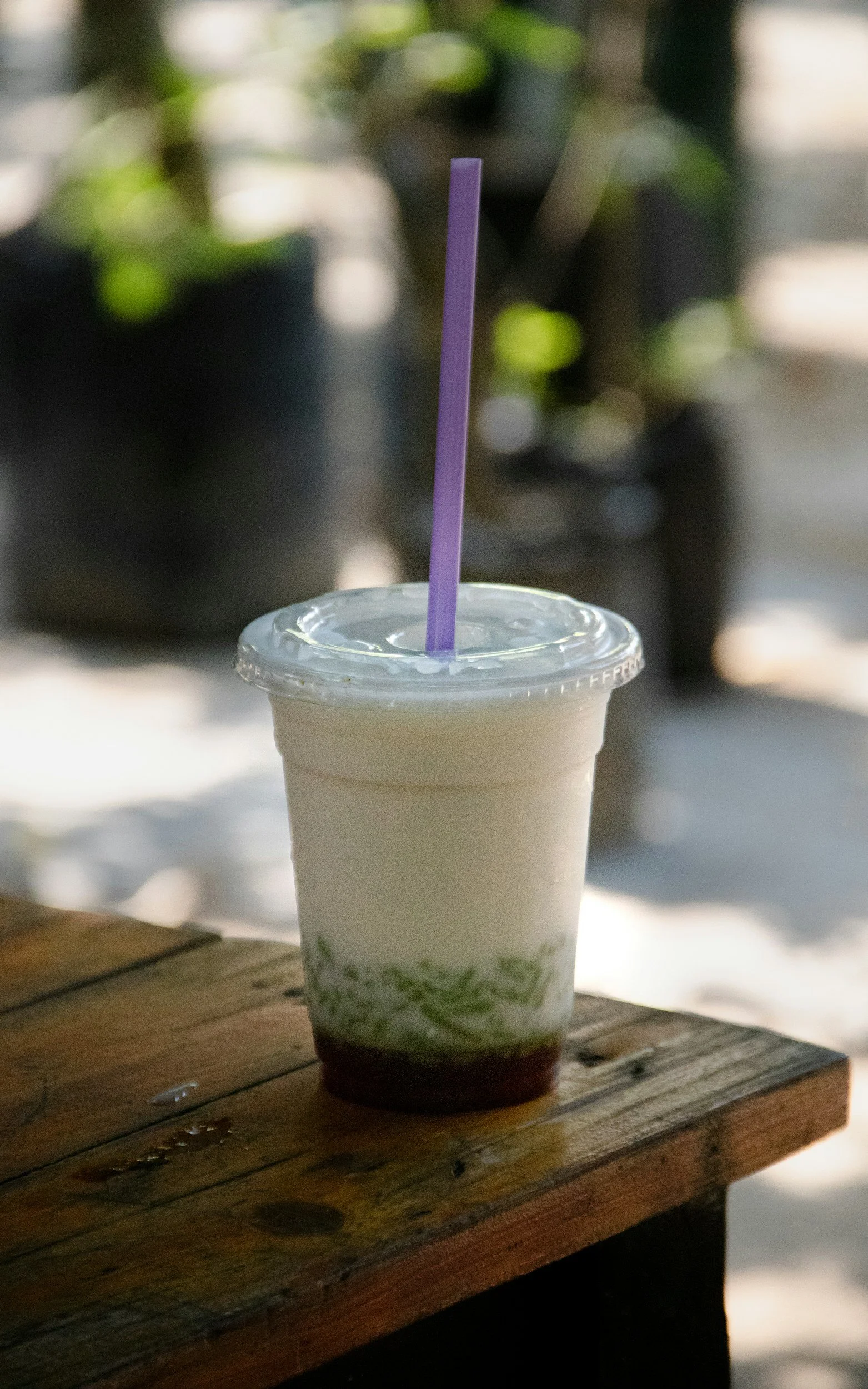 A white paper cup filled with brown tea or broth, placed on a white marble surface, next to a small pile of shiny black tapioca pearls.