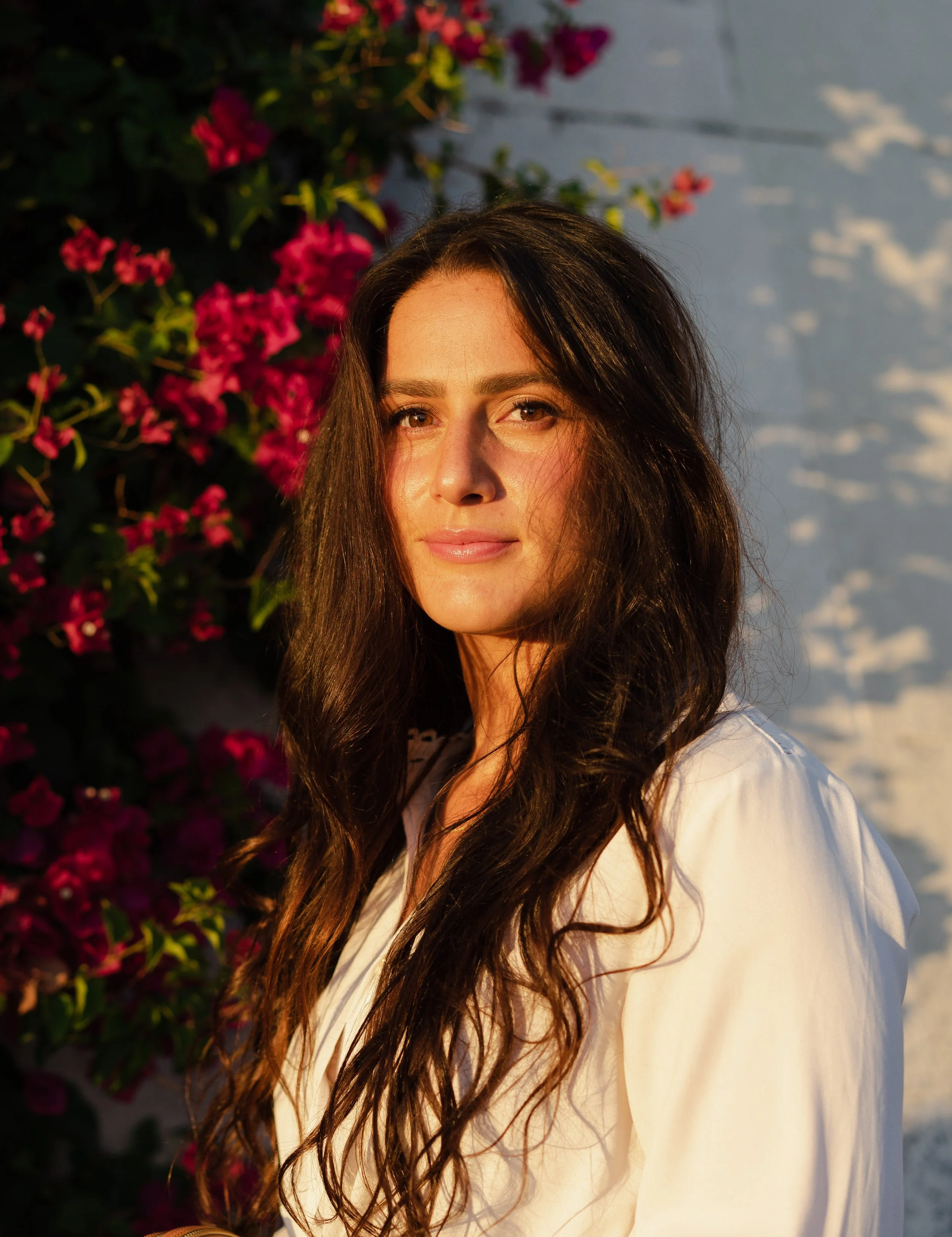 a woman with brown hair in front of bougainvillea