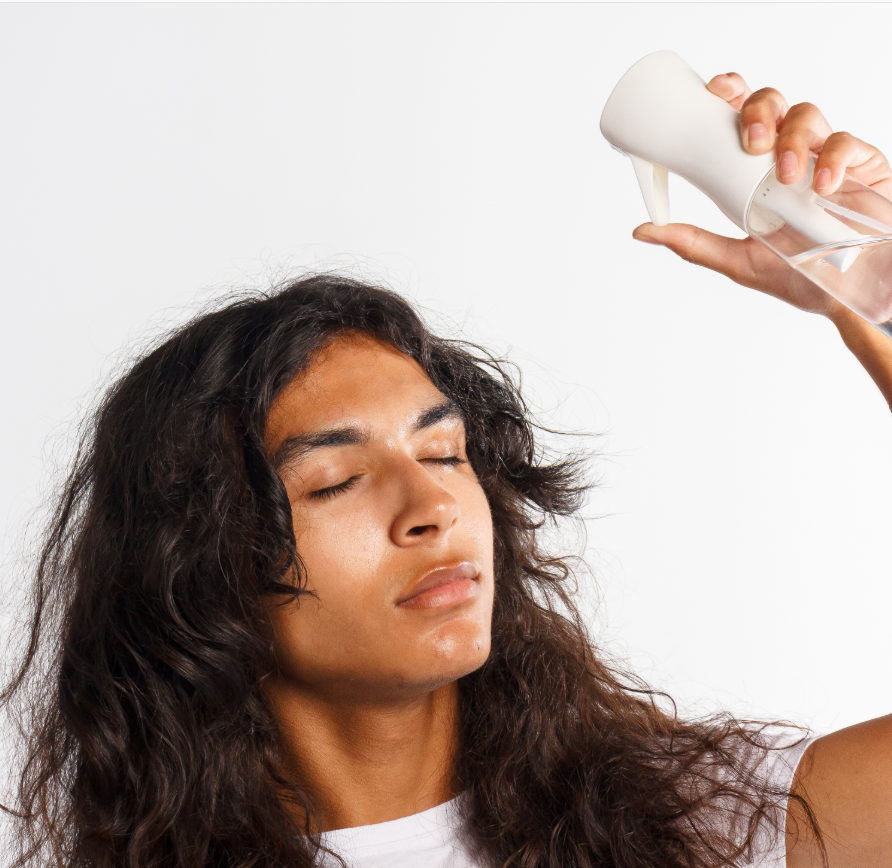 Man with curly hair has eyes closed while spraying water into his hair.