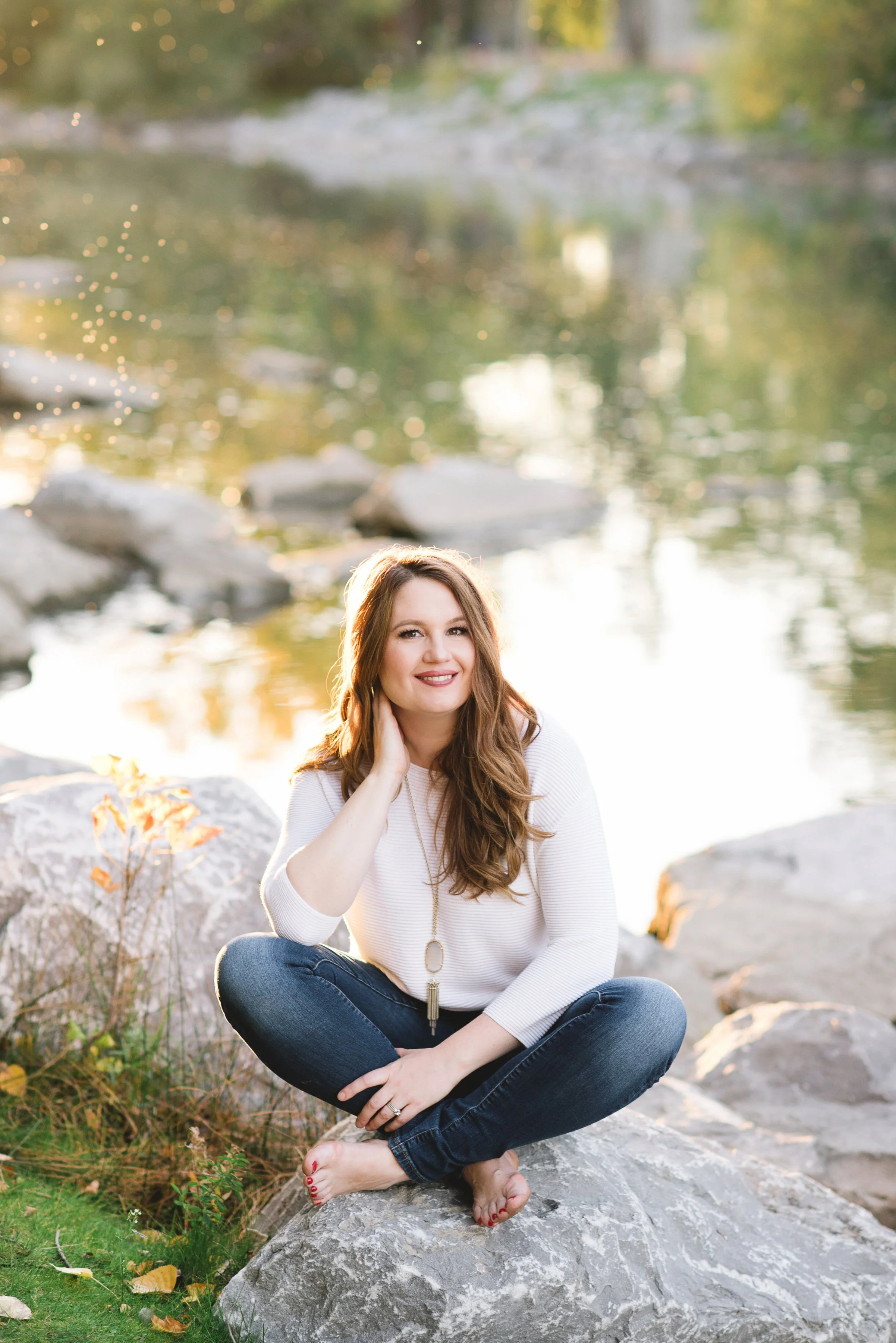 Dr. Ashley Abbs sitting cross-legged by the water – Five Element acupuncturist in Calgary
