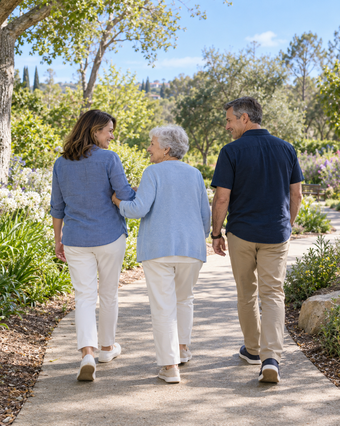 An older woman walks arm in arm with her family along a sunlit garden path.