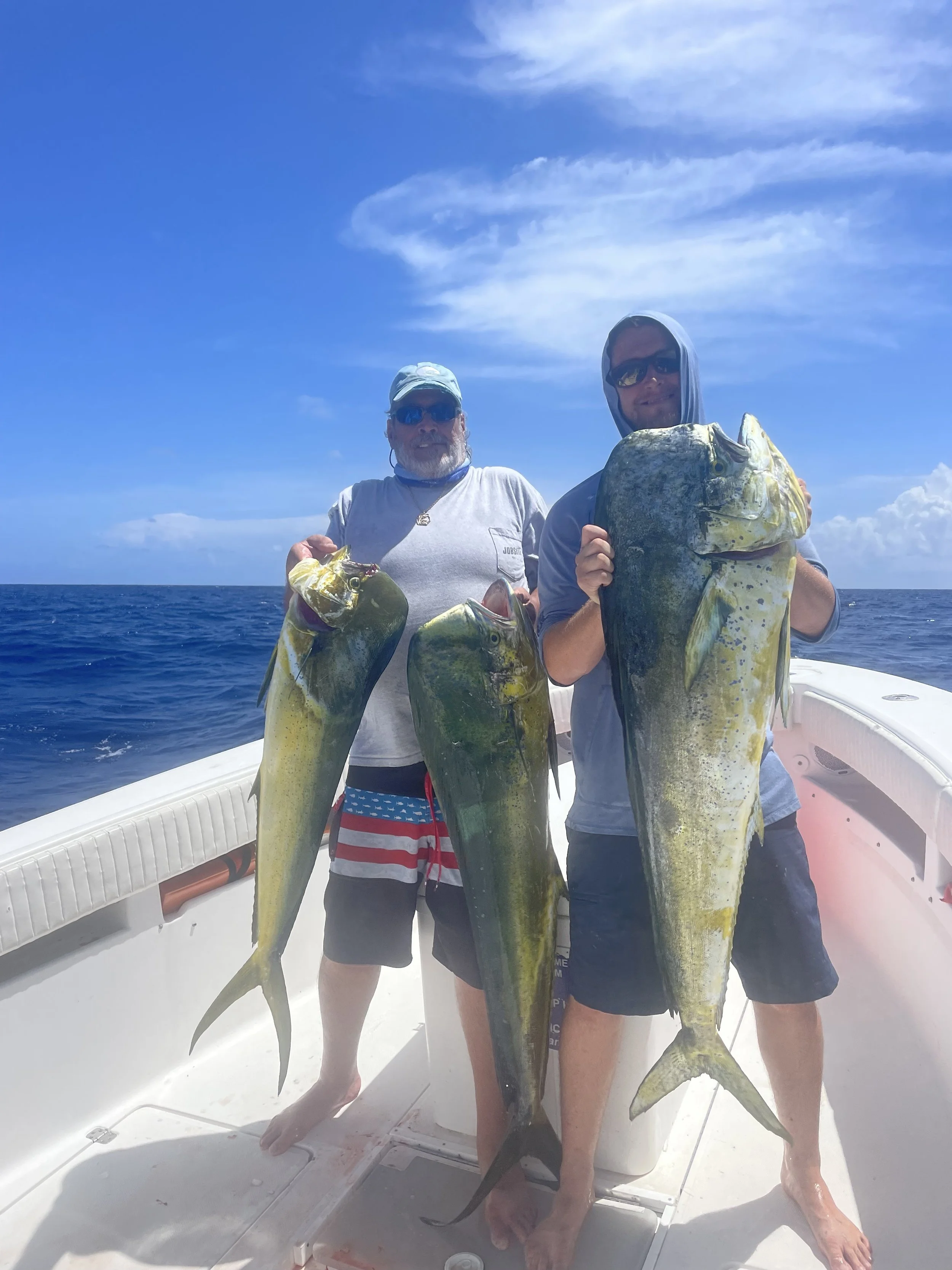 Two people holding large fish on a boat with open ocean and blue sky in the background.