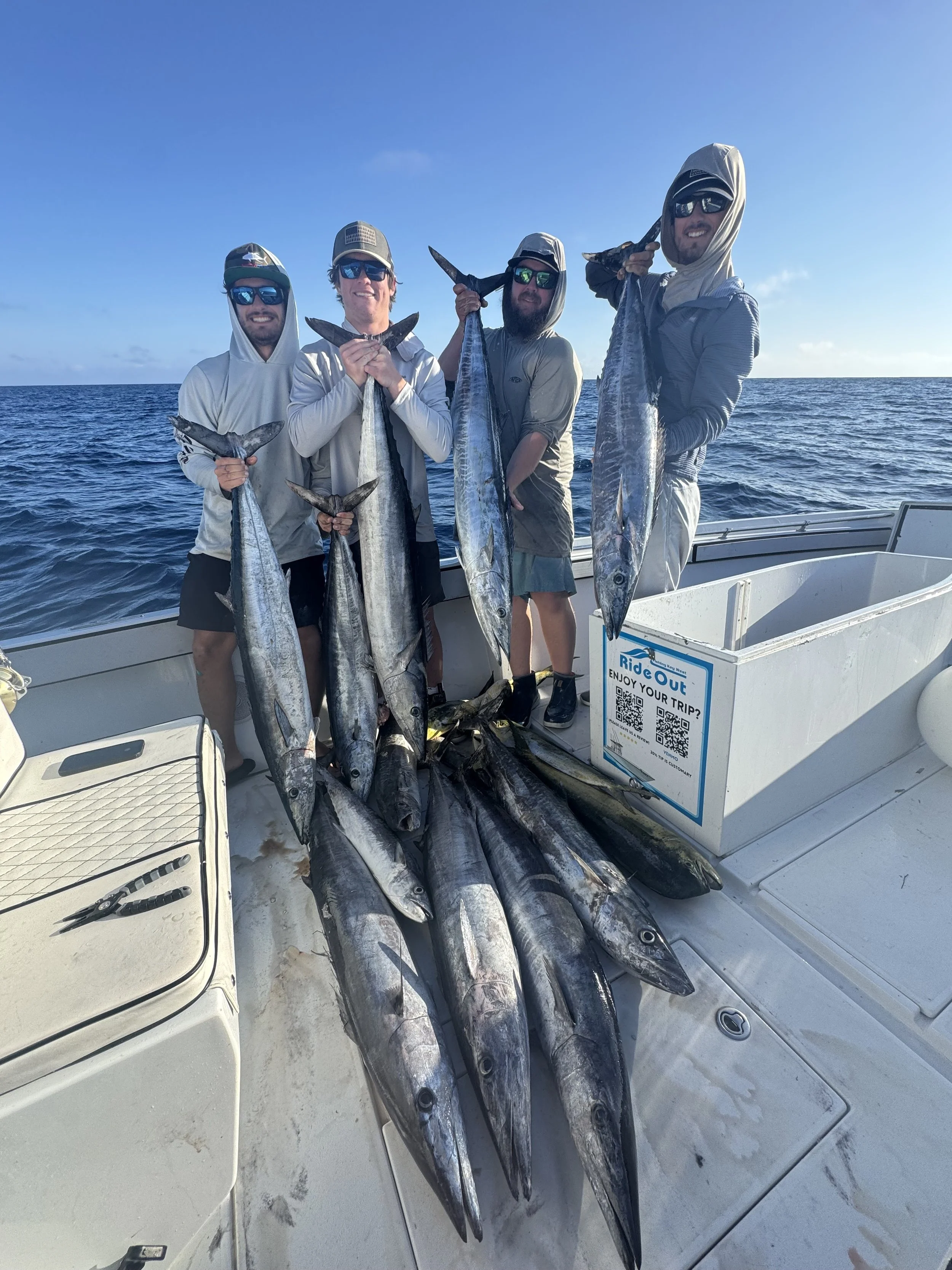 Four men on a boat holding large fish they caught, with the ocean and sky in the background.