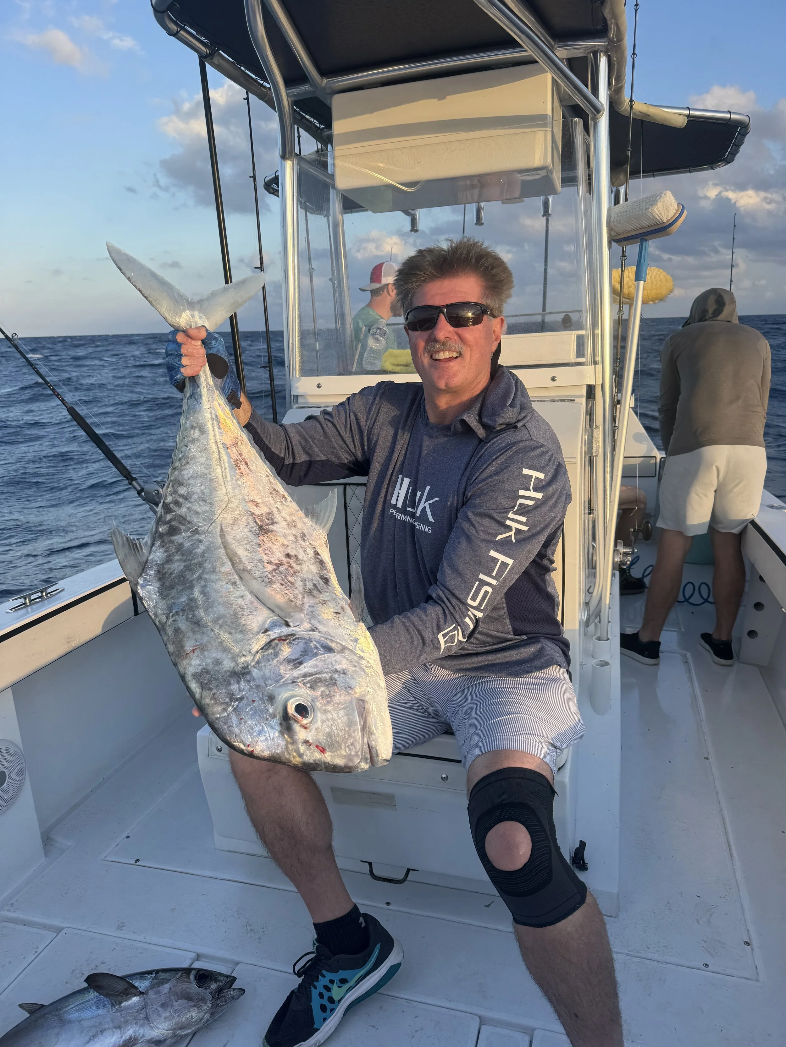 A man holding a large fish on a boat during sunset with other people in the background