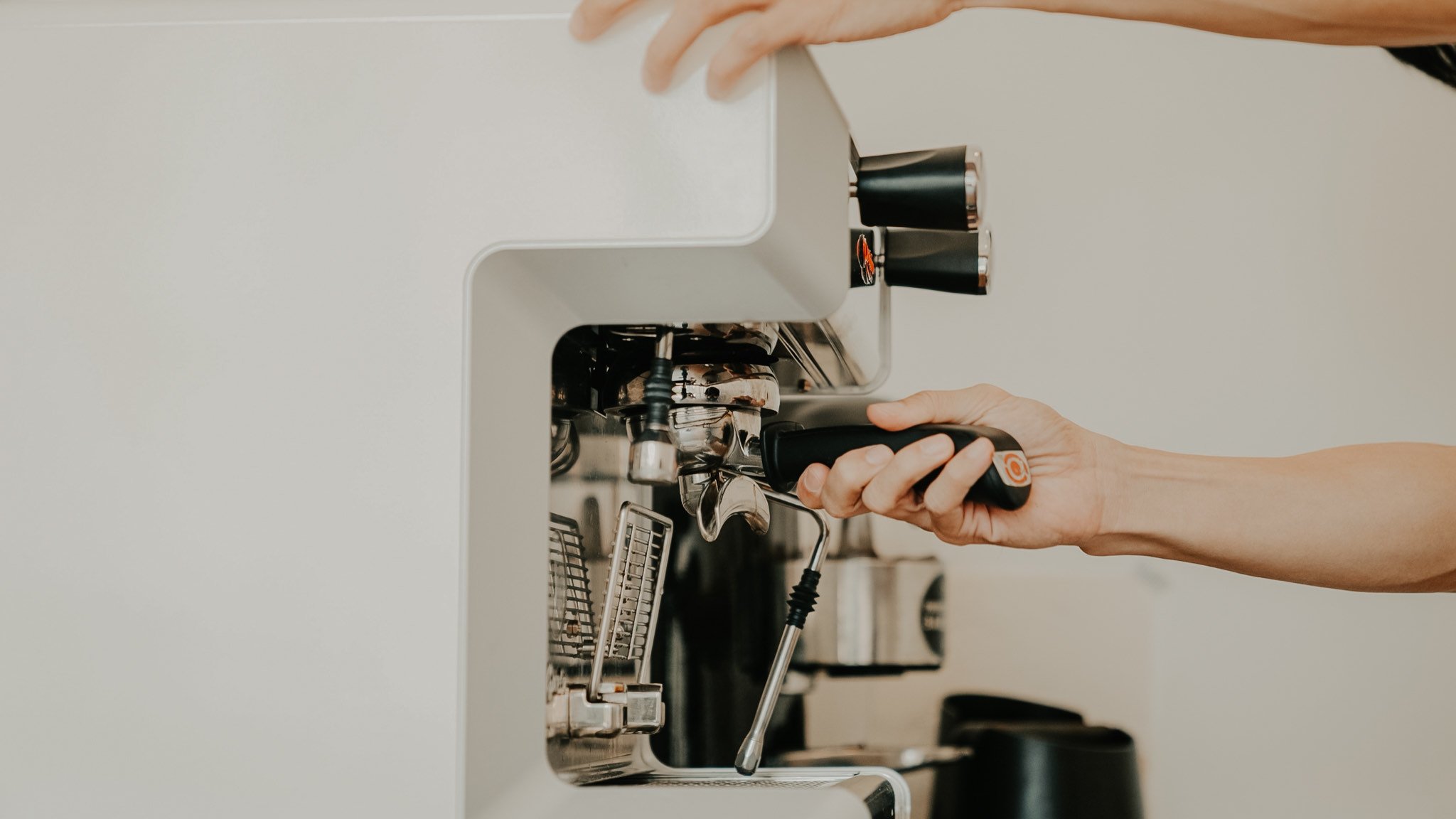A hand fitting a portafilter to a white espresso machine
