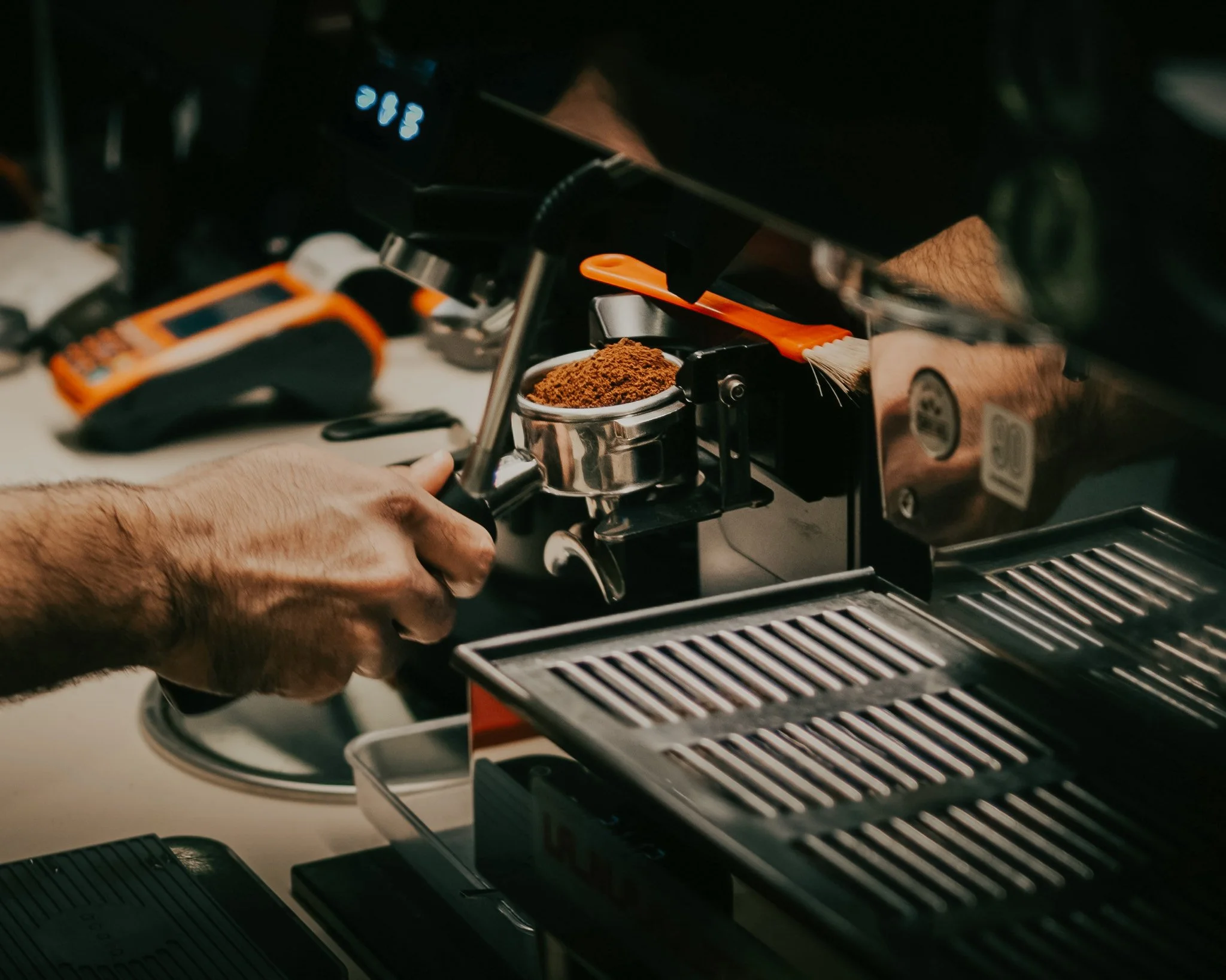 A barista tamping coffee into a portafilter at a commercial espresso machine.