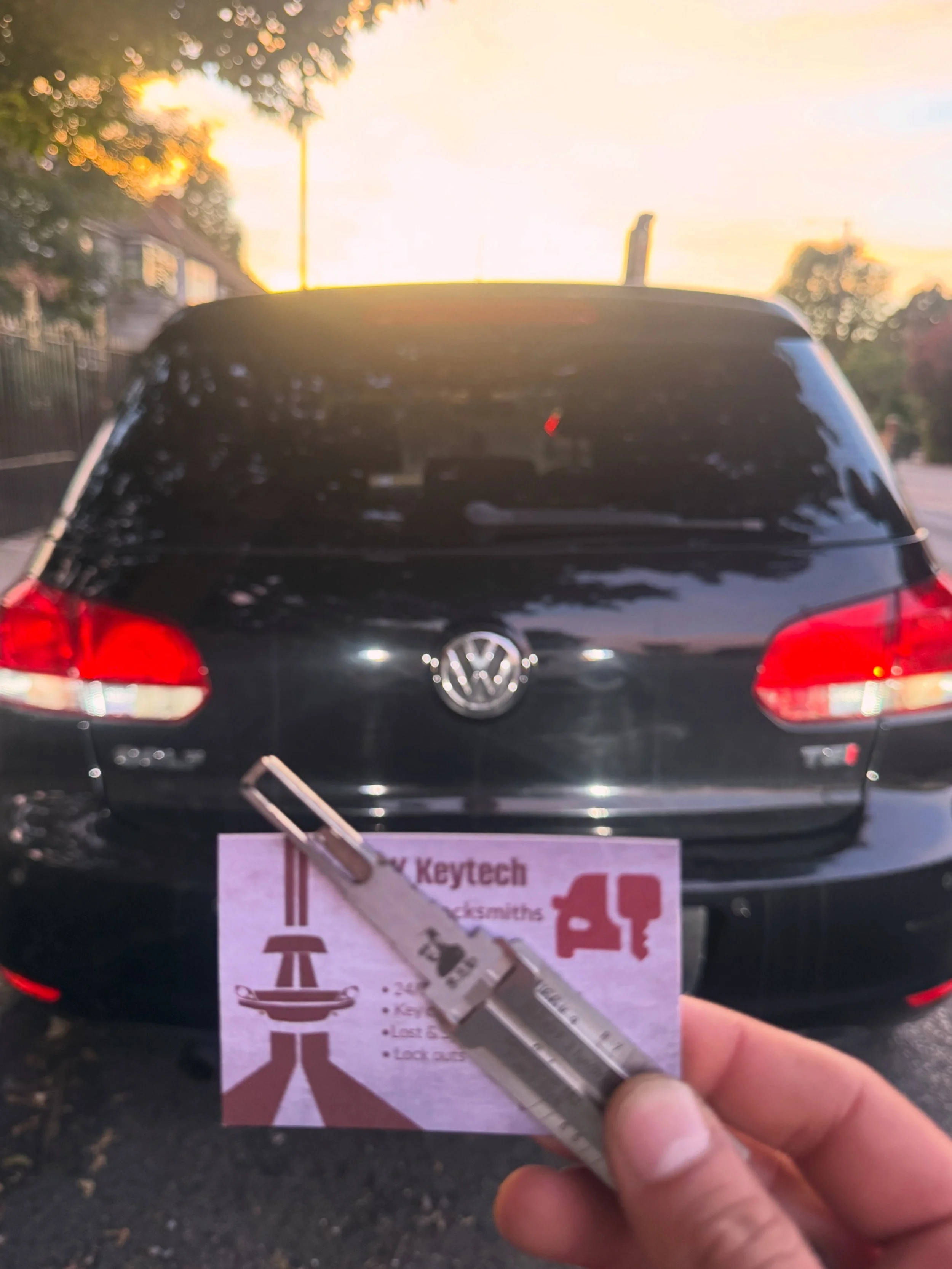 Back of a black Volkswagen car parked outdoors during sunset with a person holding a search tool and a flyer with a diagram and checklist in the foreground.