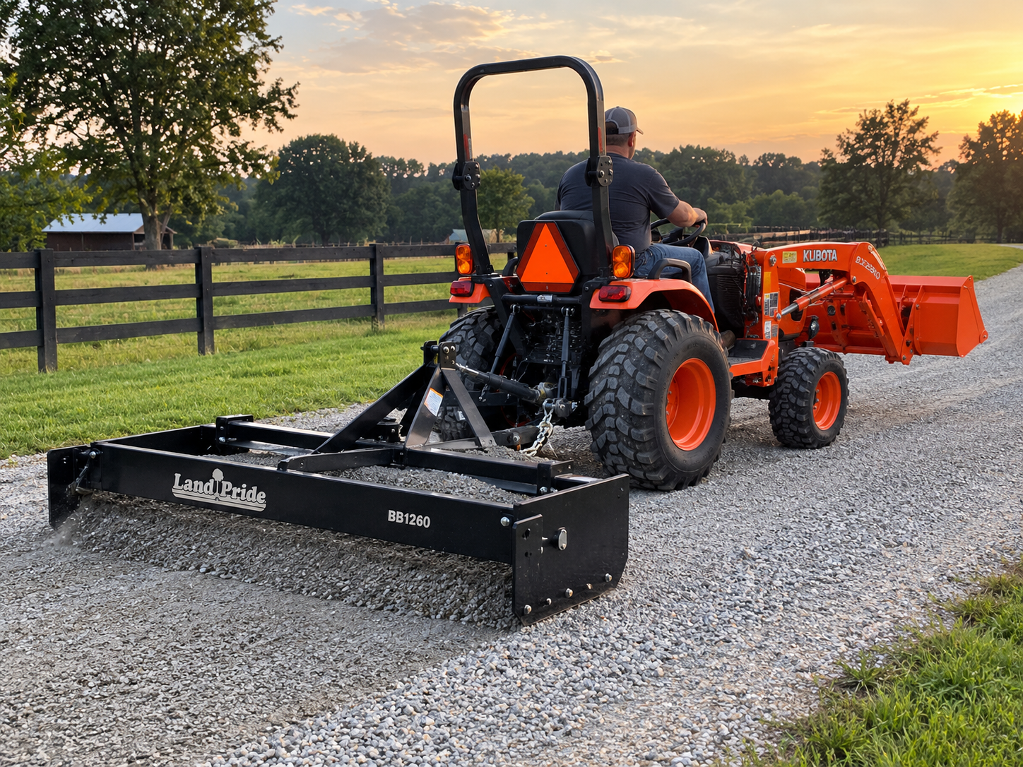 Man operating an orange Kubota tractor with a black Land Pride attachment on a gravel path at sunset, near a grassy field and a wooden fence.