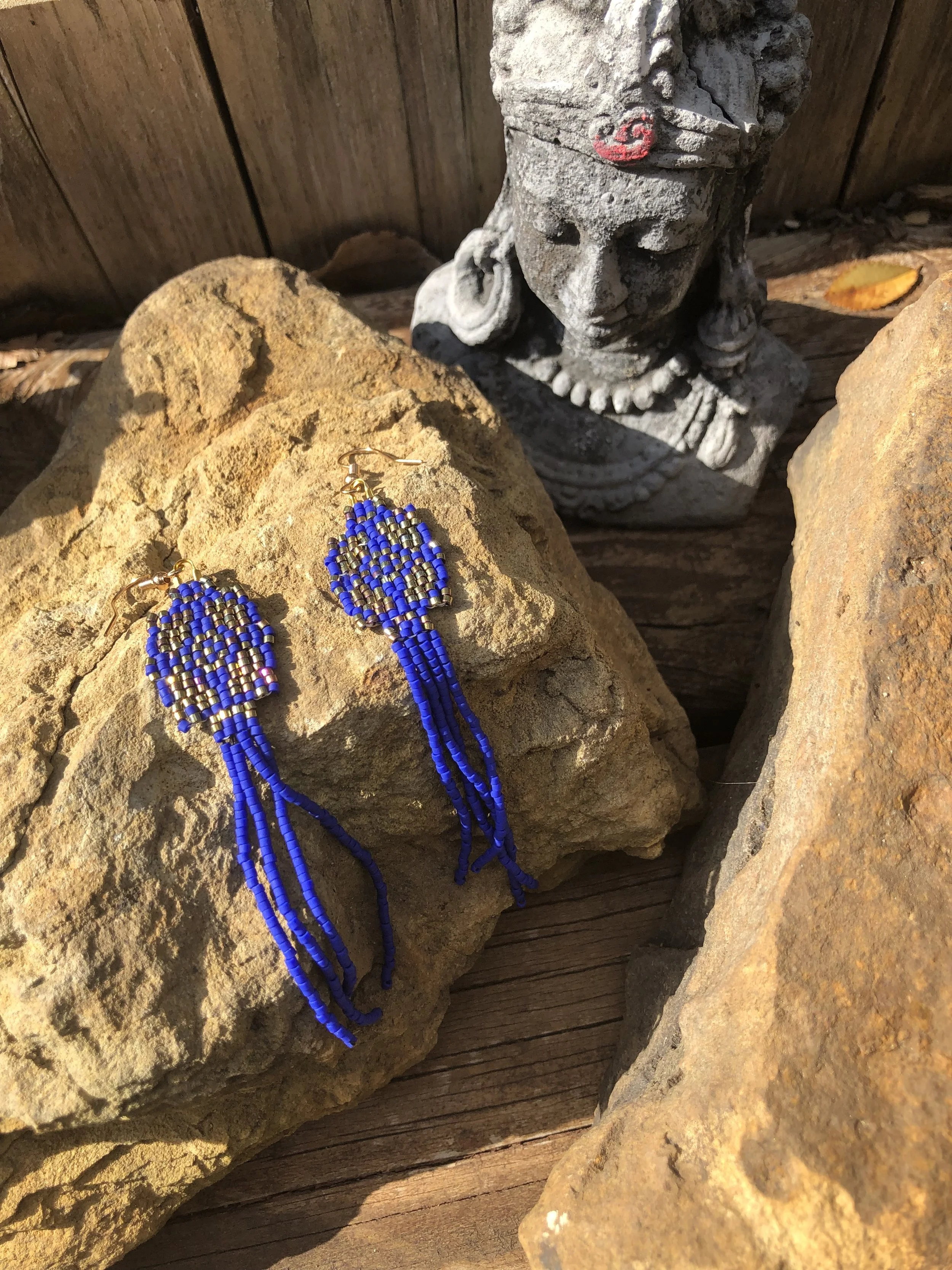 Blue beaded earrings with gold hooks resting on a large brown rock among other rocks.