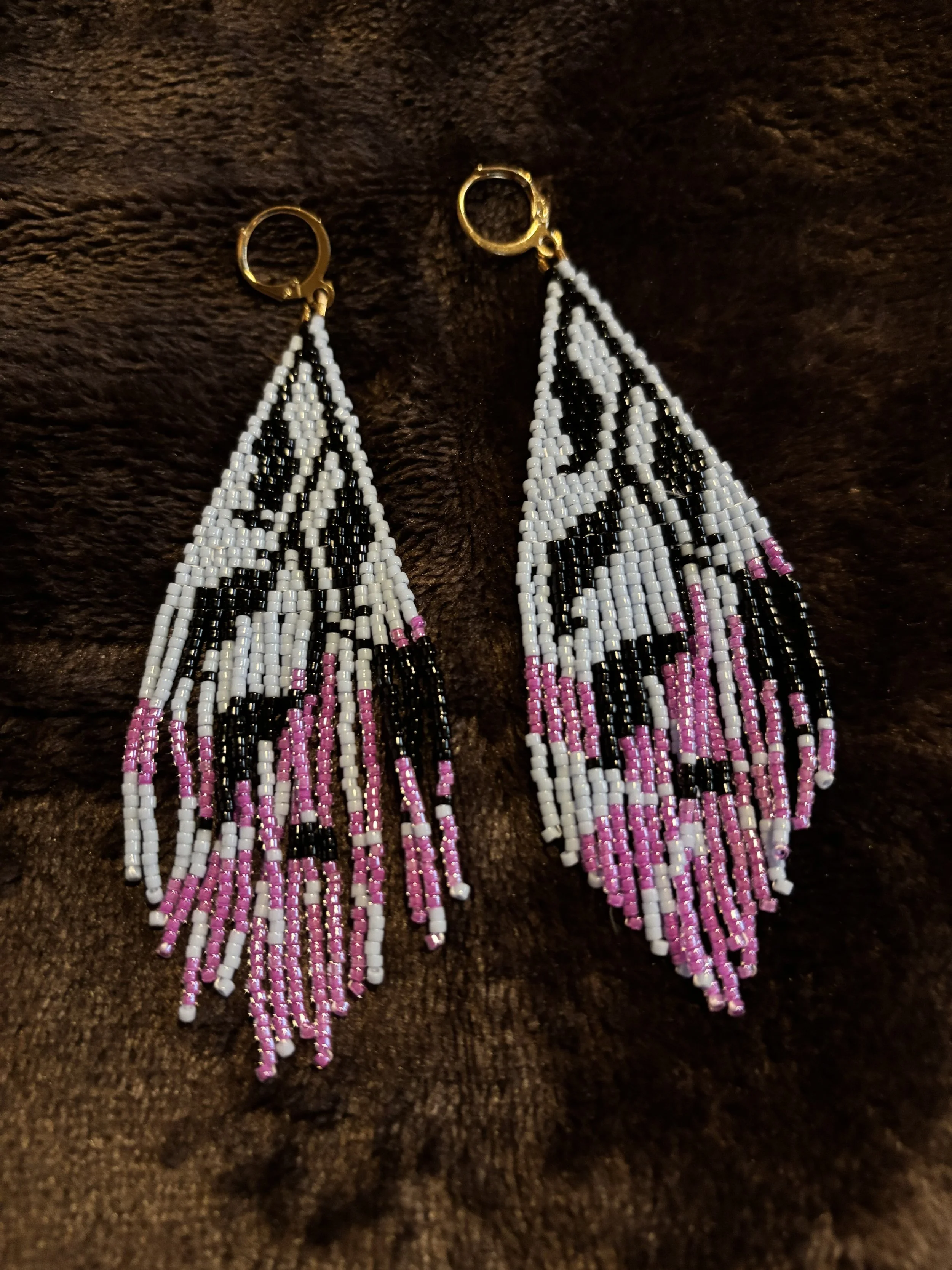 Colorful beaded earrings with pink, black, white, and clear beads hanging against a dark background.