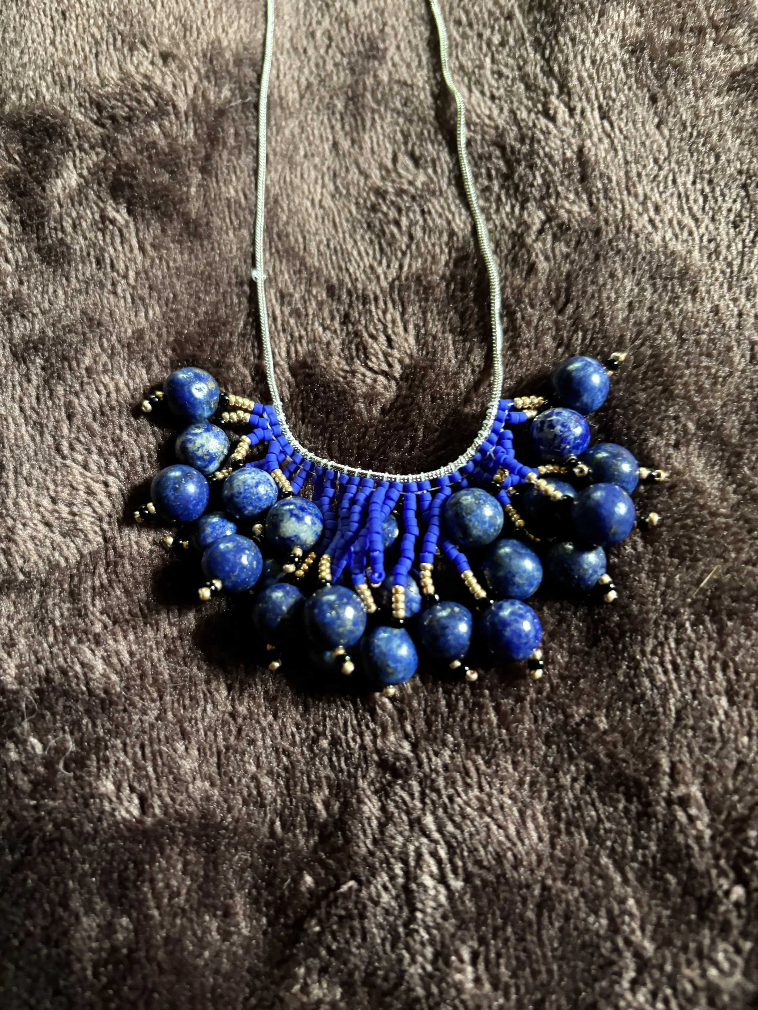 Blue beaded necklace with gold accents on a brown textured fabric background.