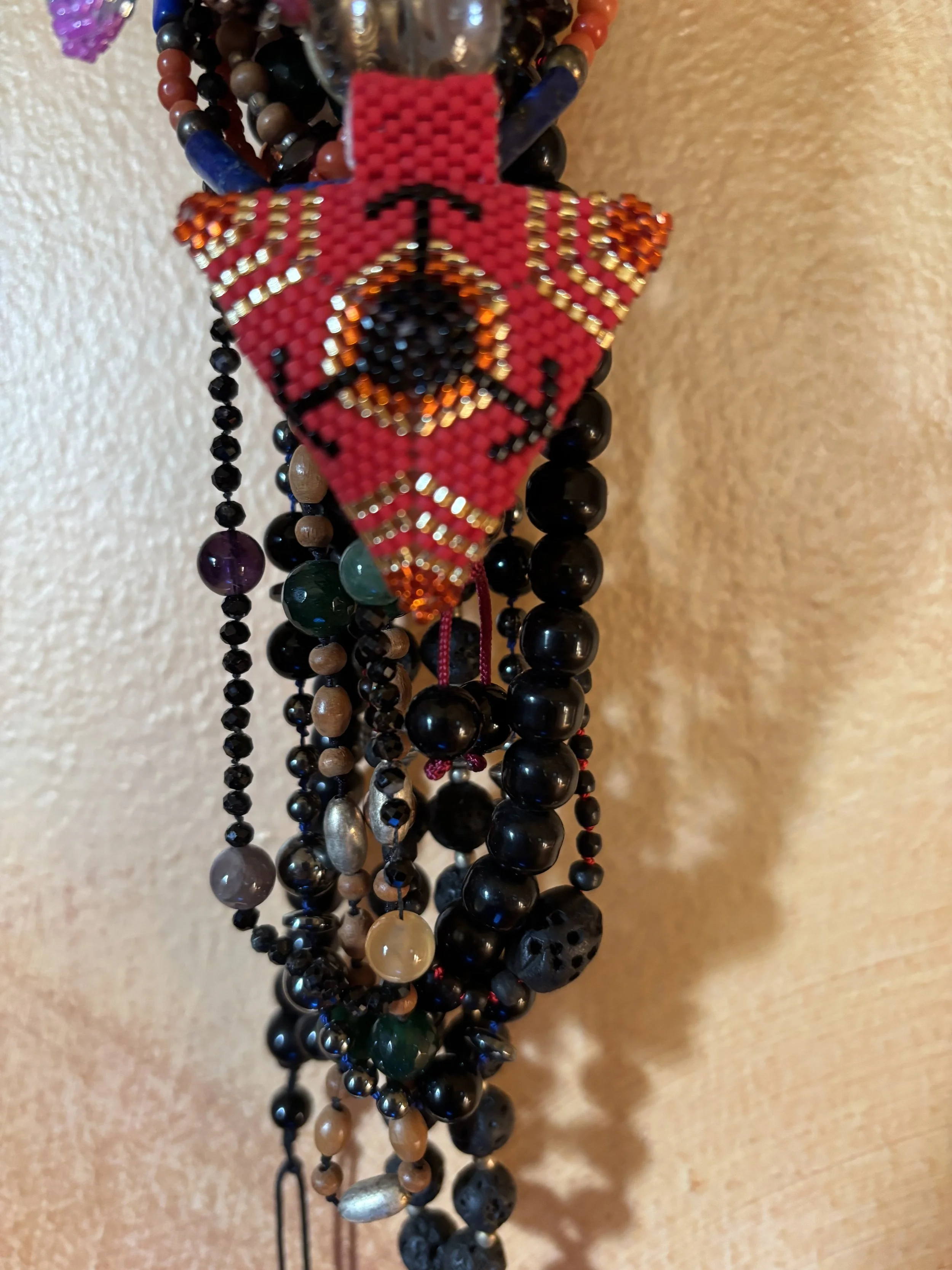 A collection of beaded necklaces hanging on a wall, with a prominent red beaded item featuring a graphic design and the word 'LOVE'.