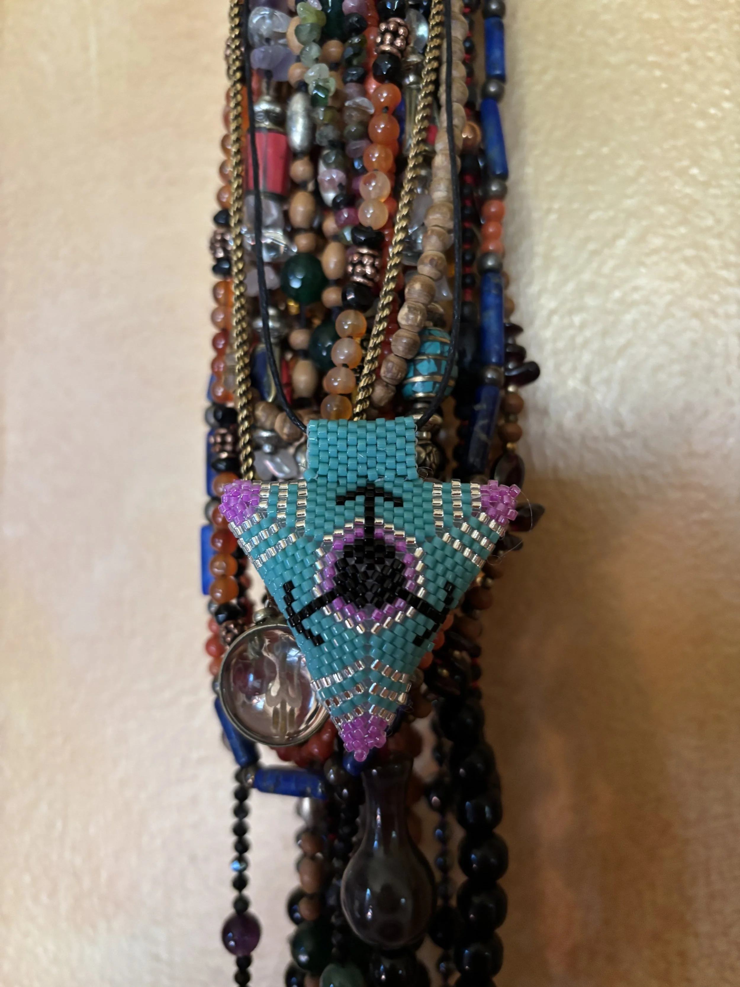 A variety of beaded necklaces and bracelets, including turquoise, pink, black, and gold beads, displayed on a wall.