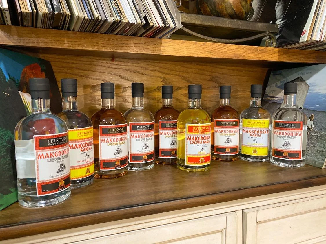 Several bottles of liquor labeled with Macedonian and Petrovsky brands on a wooden shelf.
