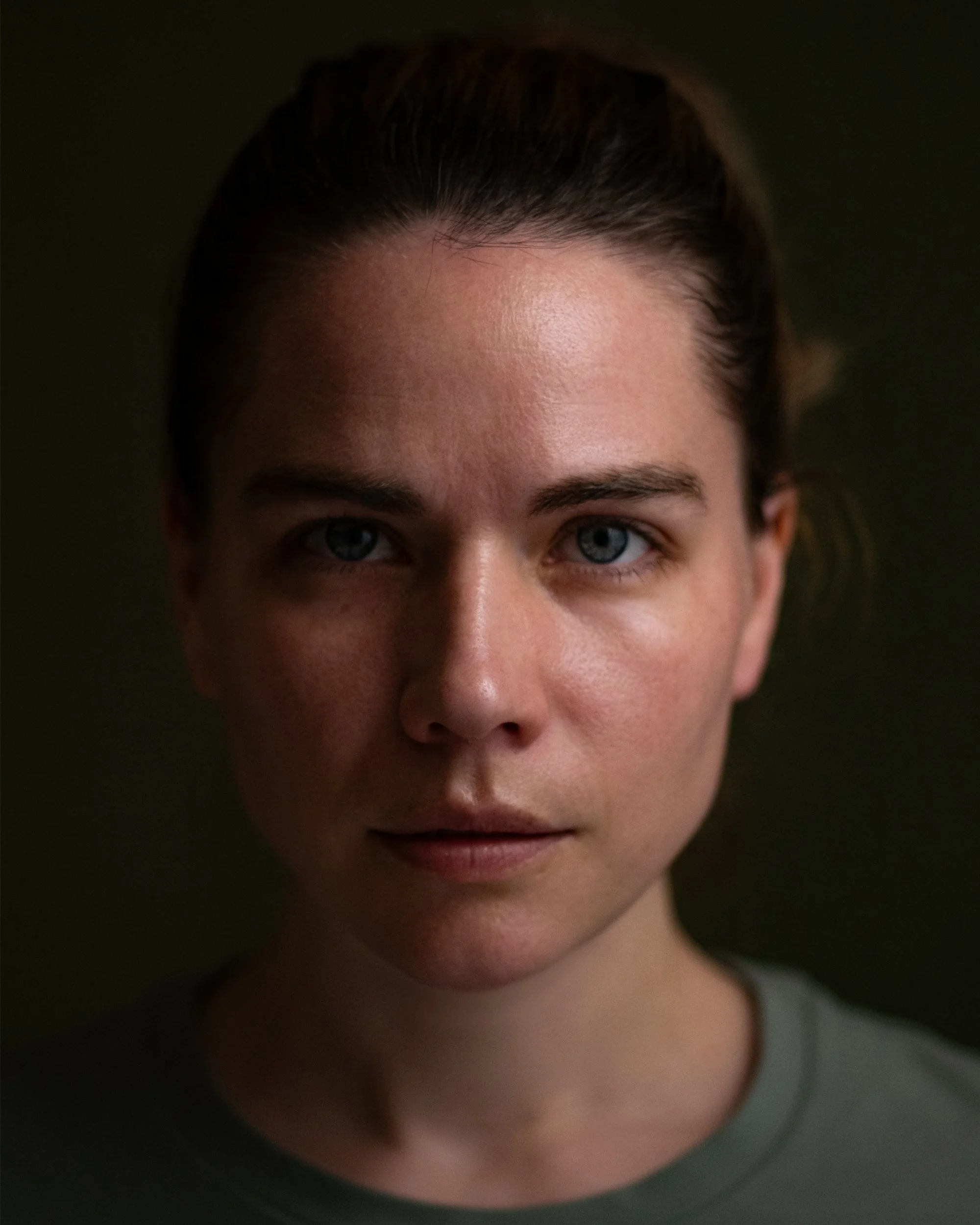 Jennifer Mcd. Writer & Producer. Close-up of a woman's face with blue eyes, dark hair pulled back, and a neutral expression, with a dark background.