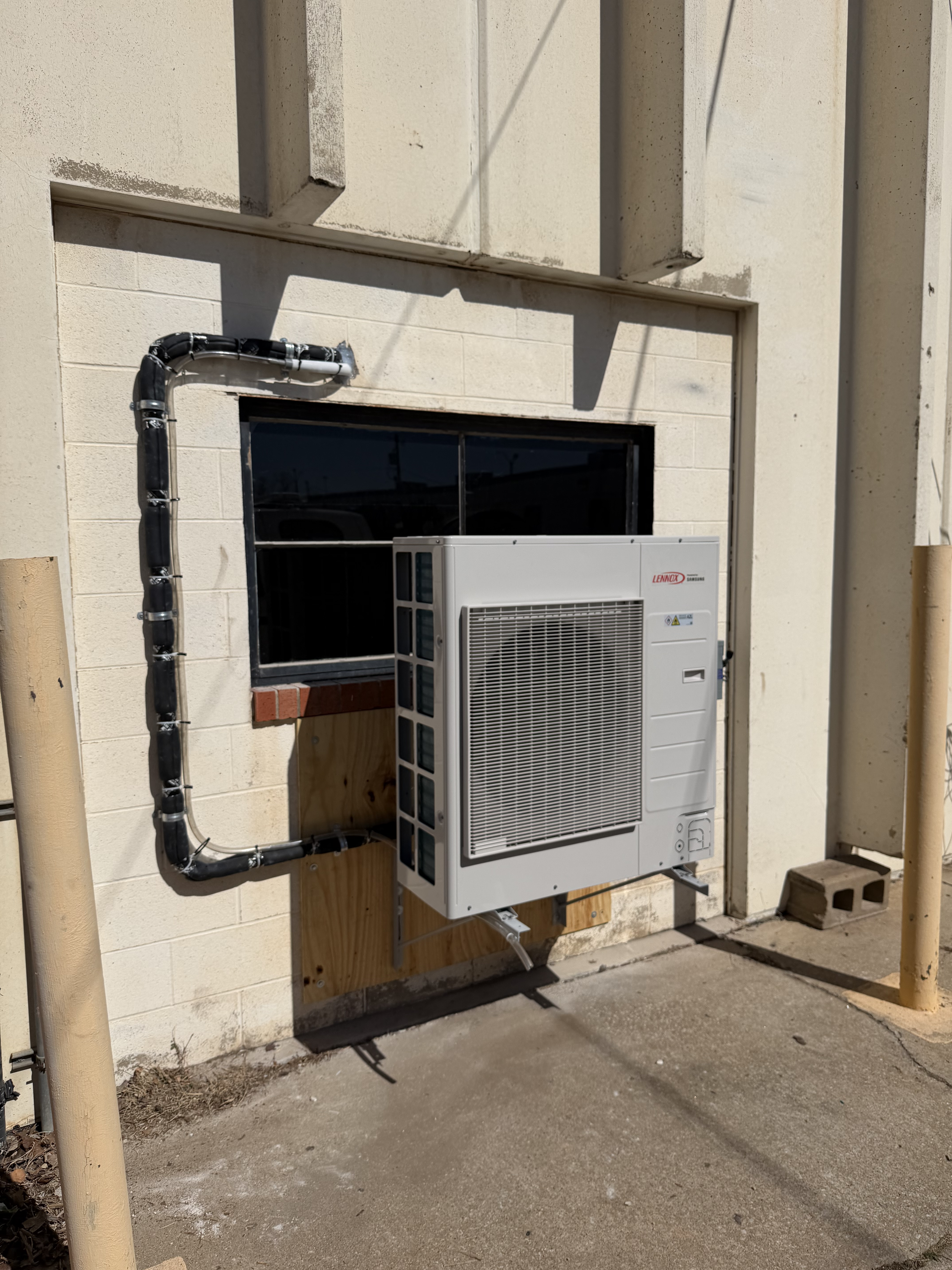 Exterior wall with an air conditioning unit installed, with visible piping and wiring.