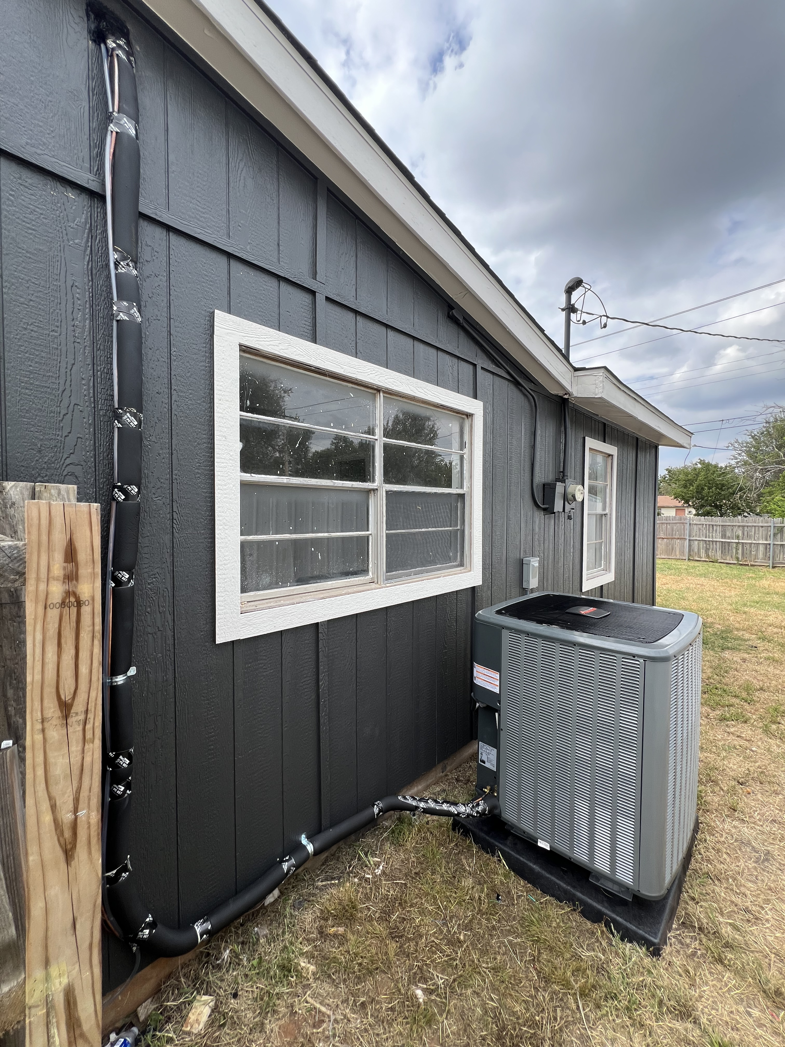 Exterior of a house with black siding, white trim around the windows, and an HVAC unit on the ground outside.