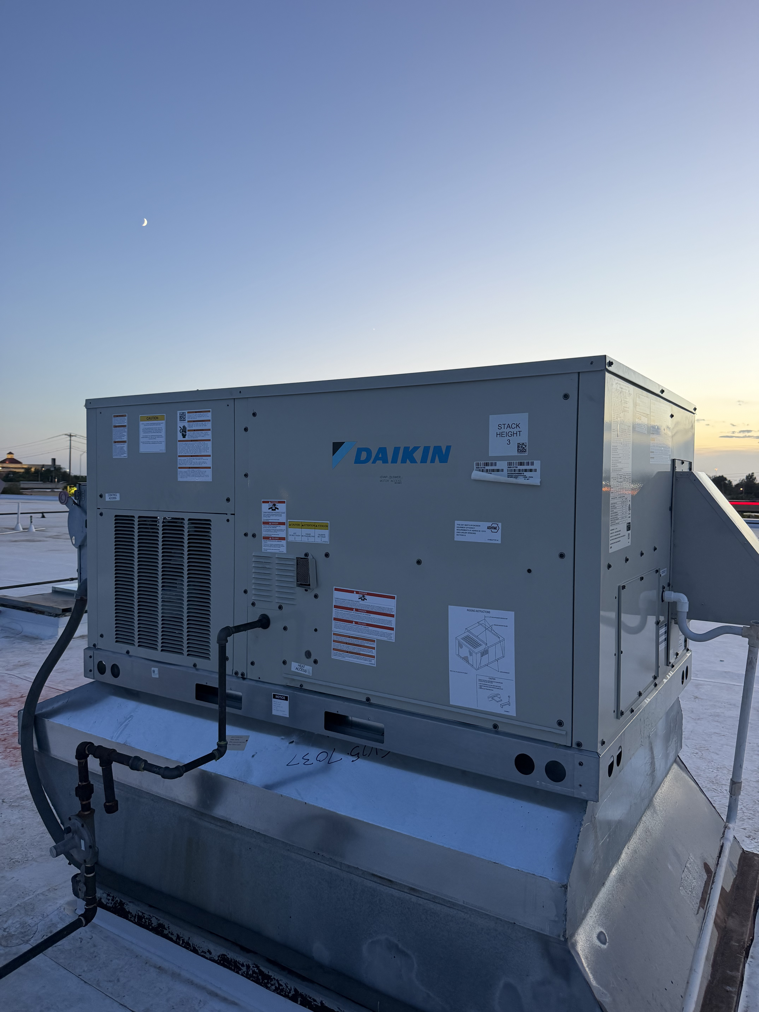 Commercial HVAC unit by Daikin installed on a rooftop with a clear evening sky, visible crescent moon, and power lines in the background.