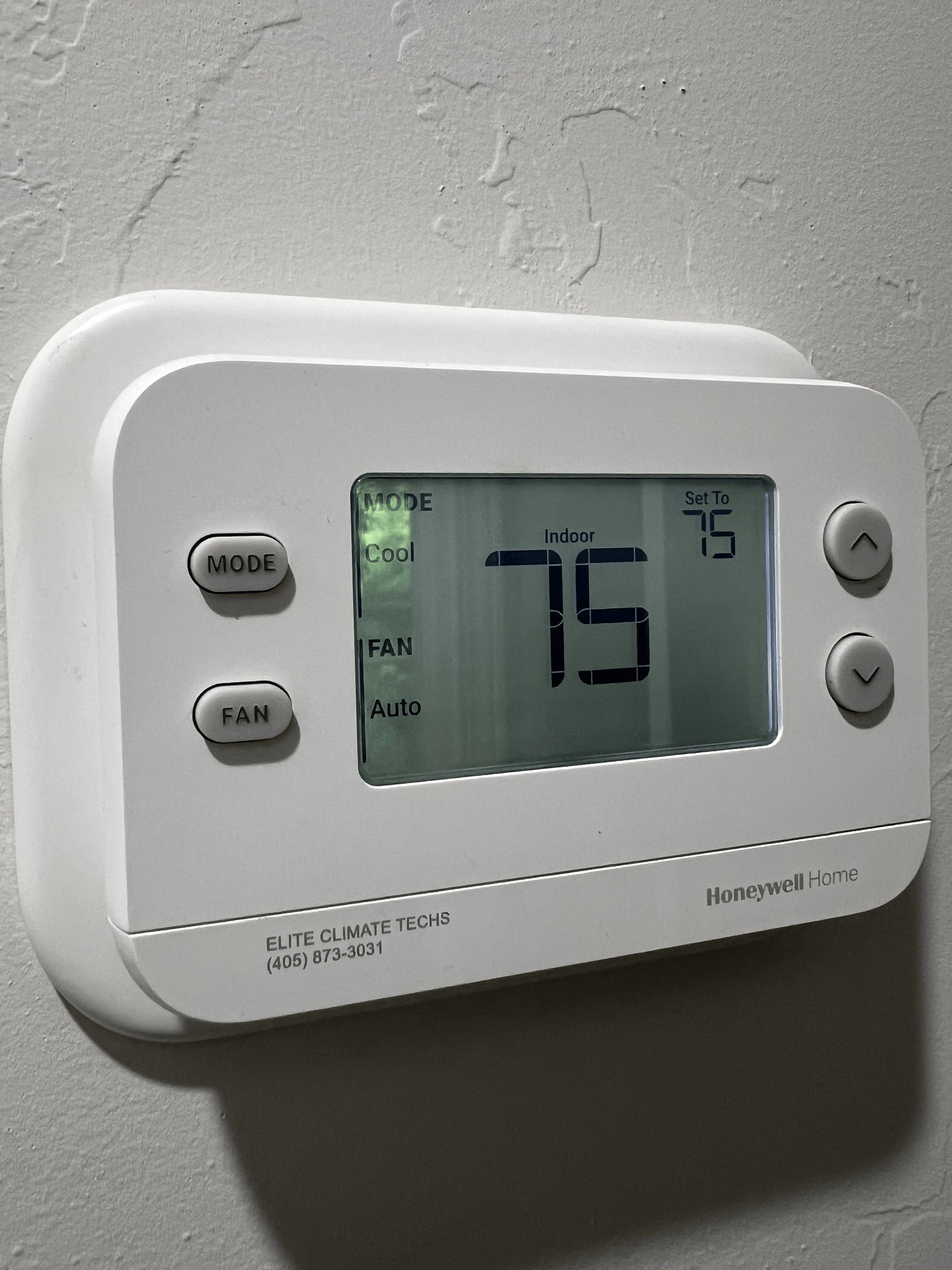 A white Honeywell Home digital thermostat mounted on a gray wall, displaying a temperature of 75 degrees Fahrenheit and set to indoor cooling mode.