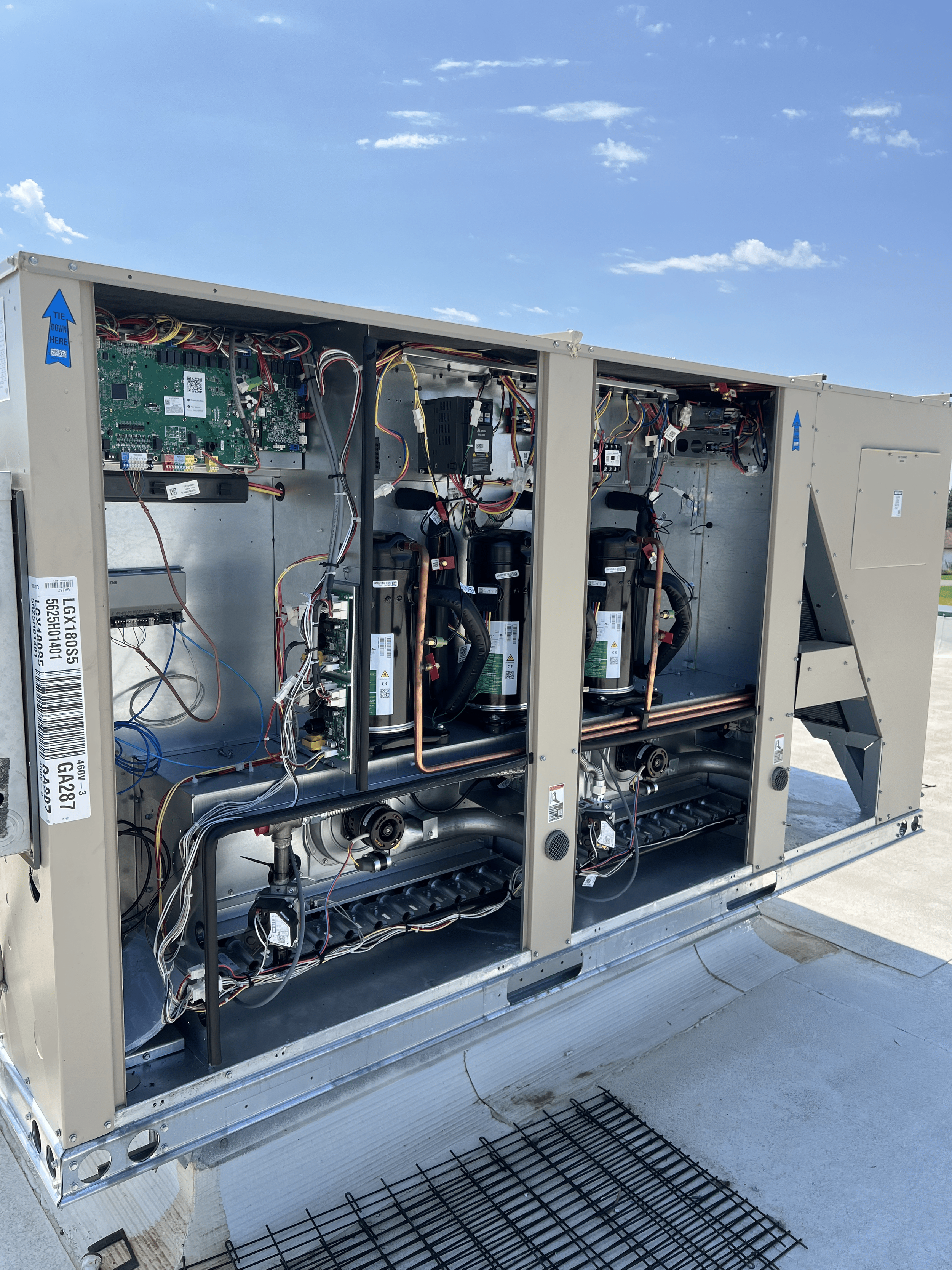 Open HVAC unit with internal components and wiring, viewed outdoors against a sky with clouds.