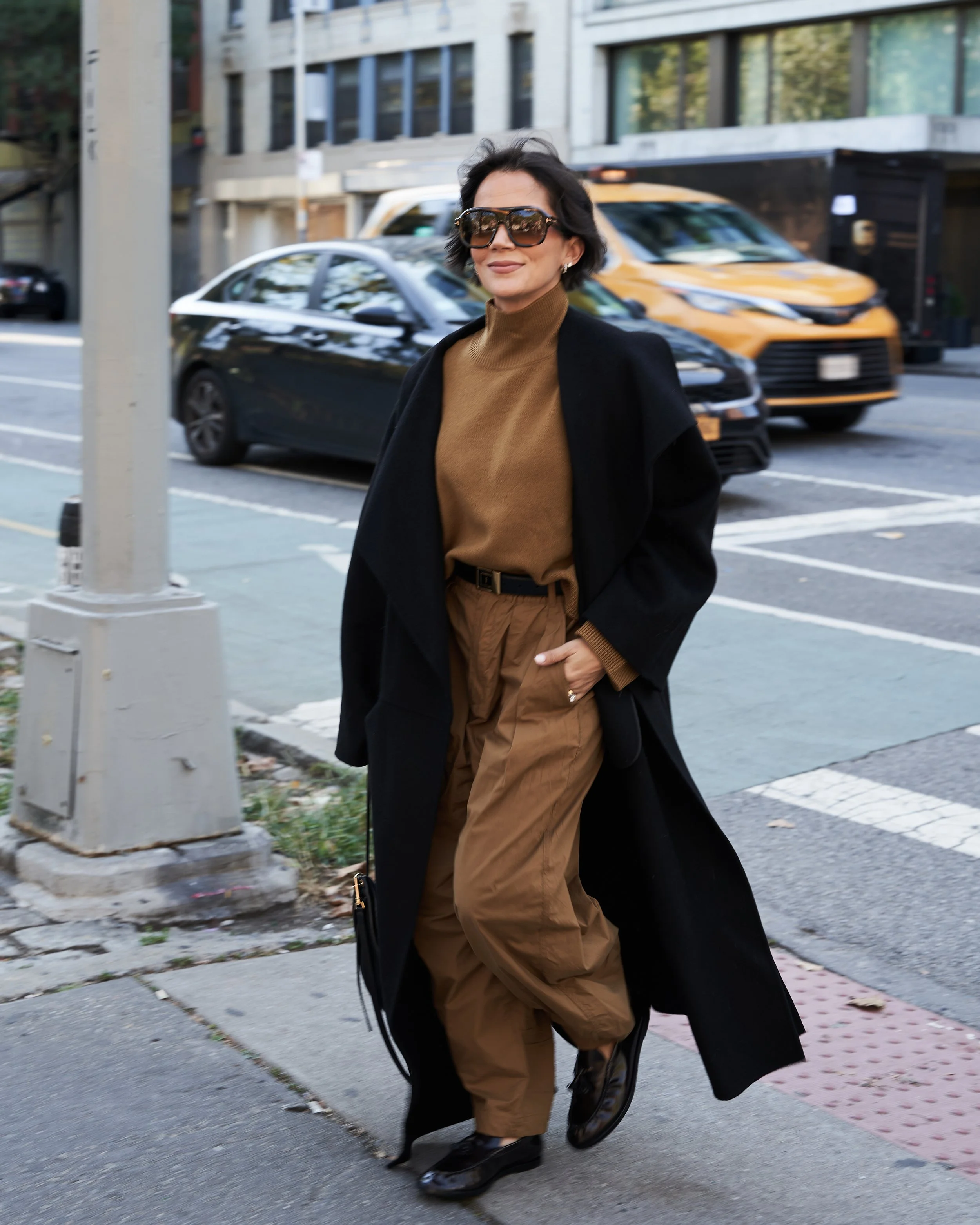 Melissa of Styled by Meeshamore in a camel suit and long black coat on a city street, travel styling