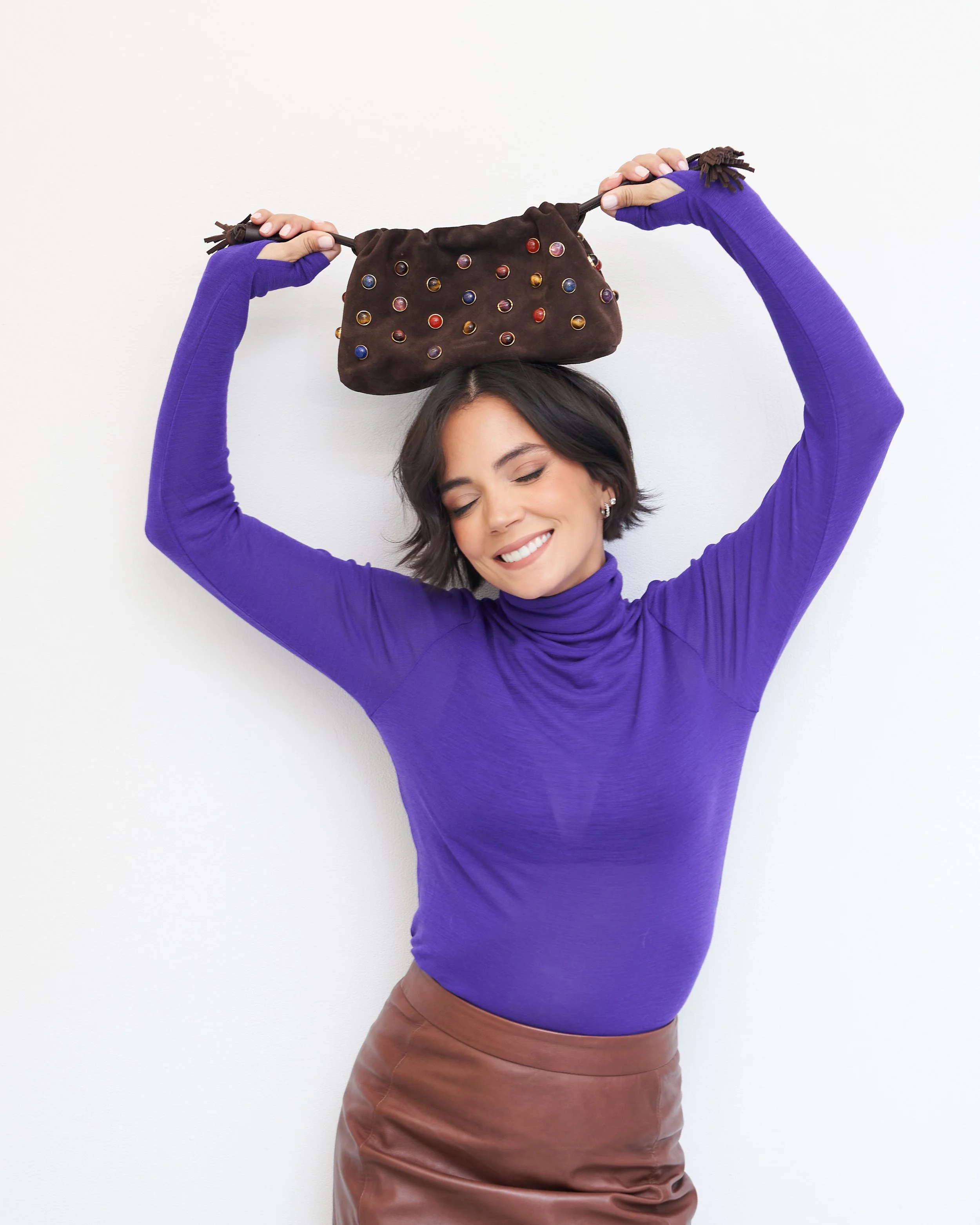 Violet turtleneck with a brown leather skirt and a beaded handbag held overhead