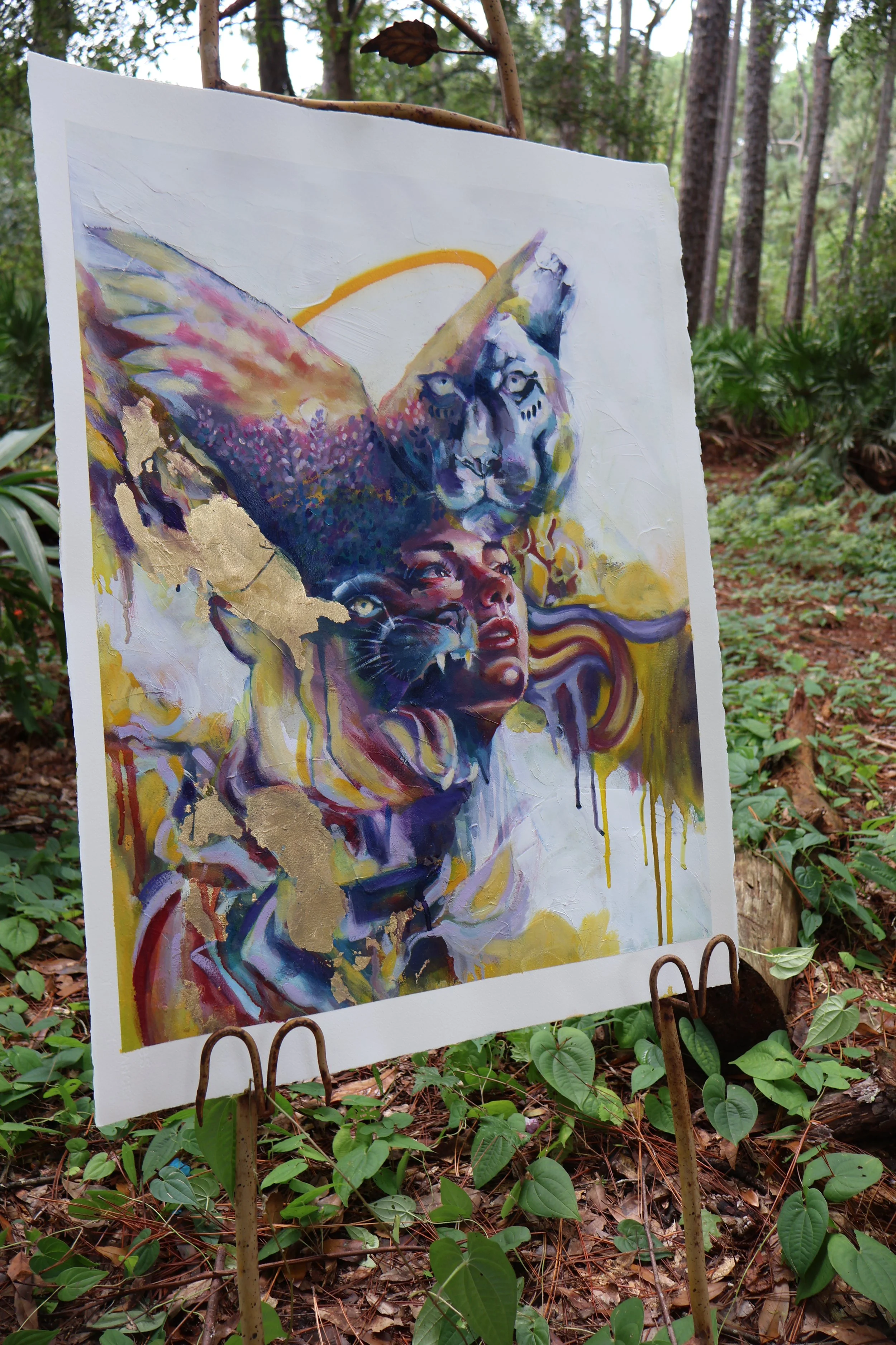 Colorful abstract mixed-media painting of overlapping faces displayed on an easel in a forest