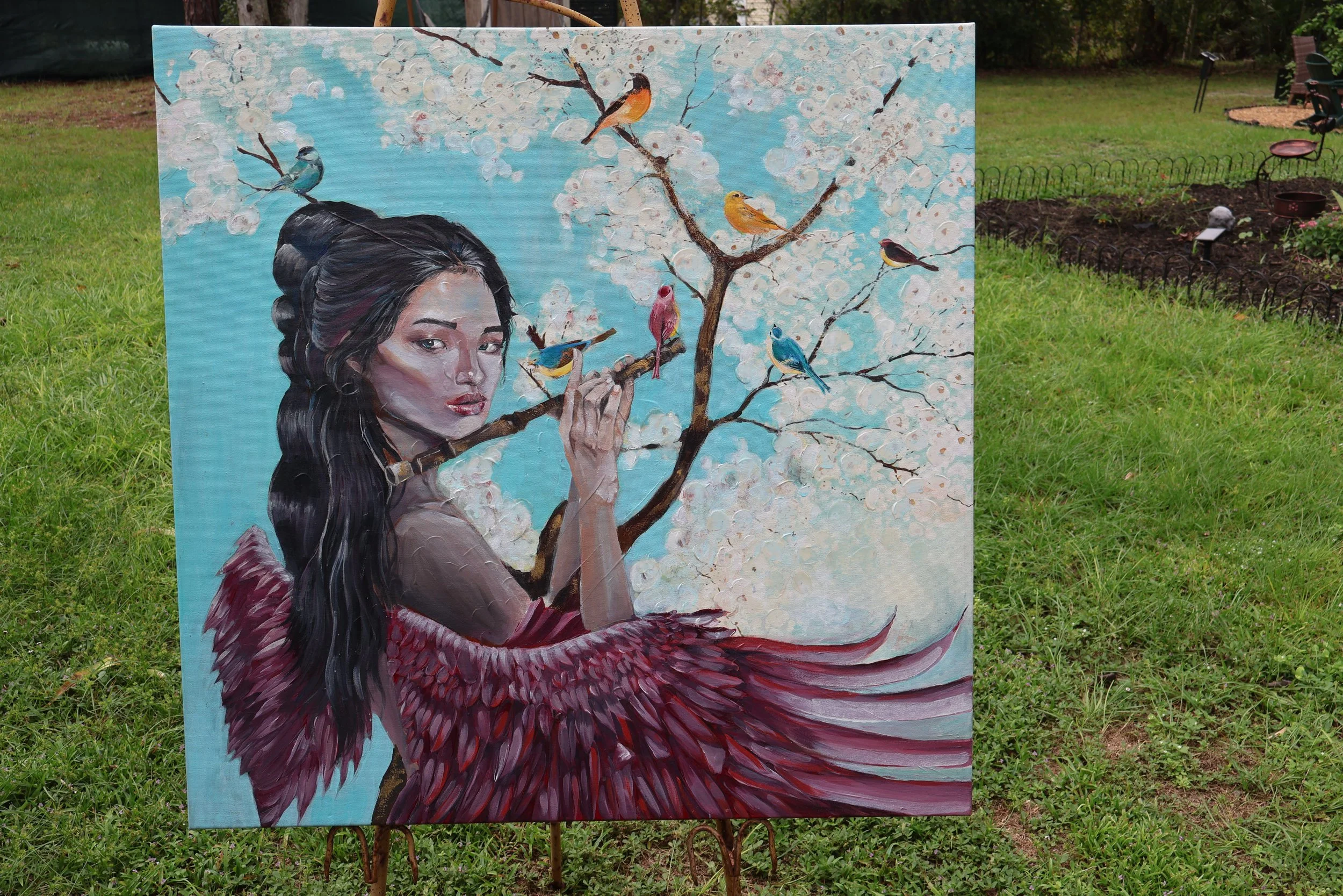 Outdoor painting of a woman in a burgundy feathered dress playing a flute beneath blossoming branches surrounded by colorful birds