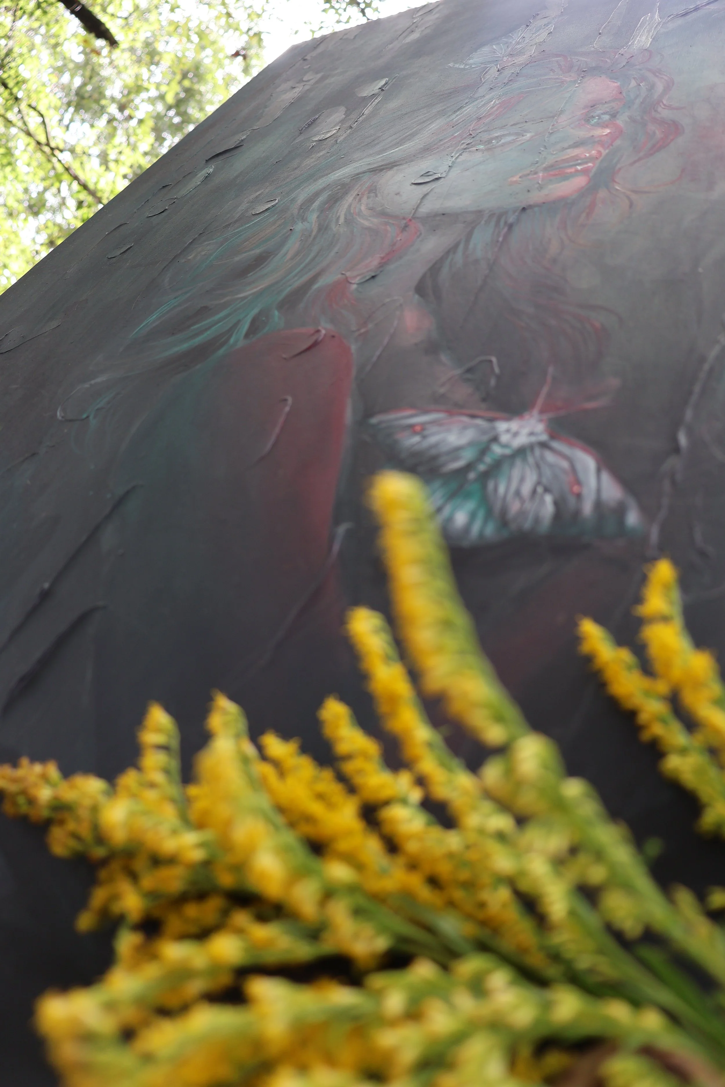 Close-up of a colorful painted mural with yellow-green foliage in the foreground