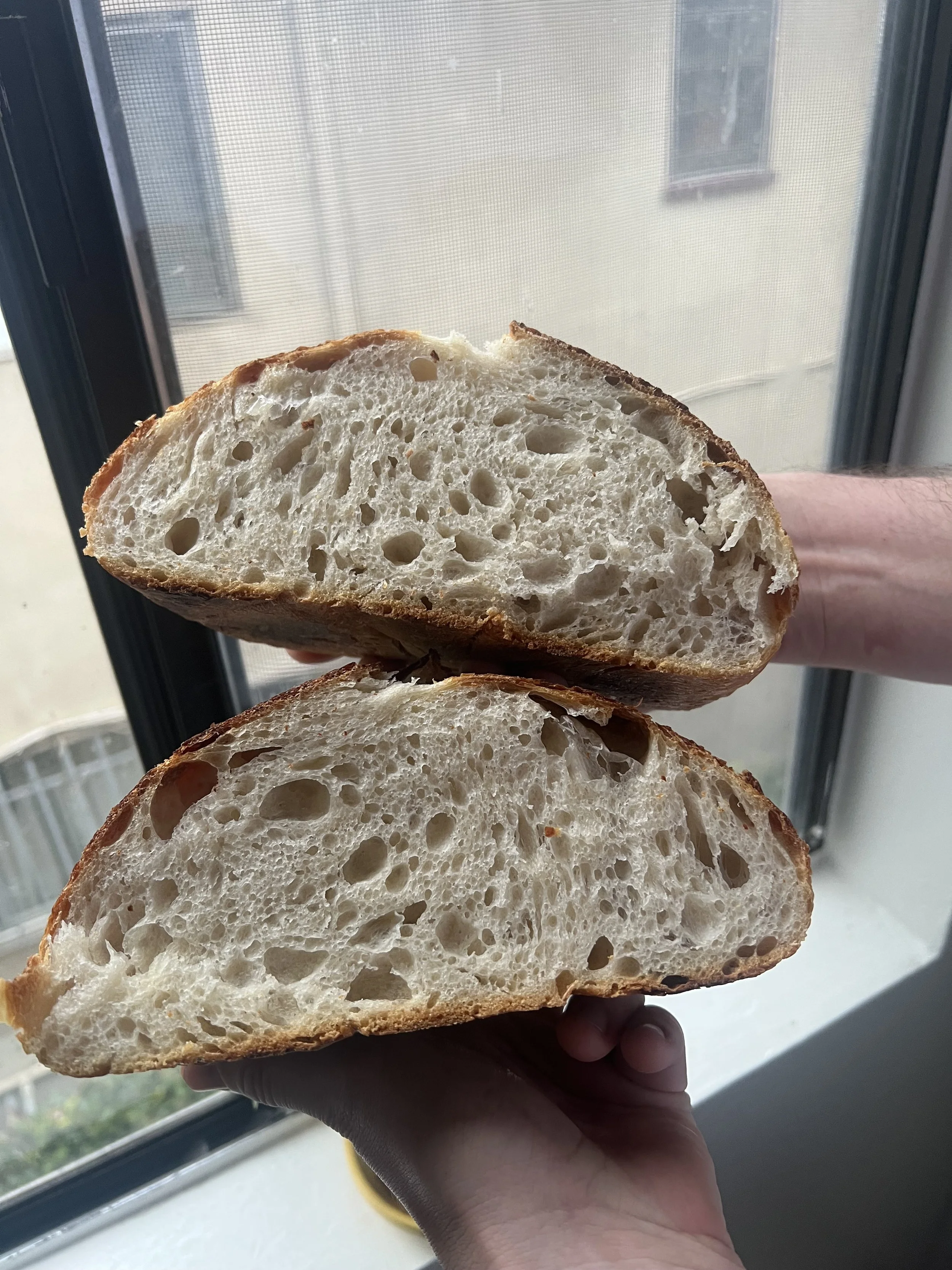 Close-up of a sliced loaf of bread with a fluffy, hole-filled interior, held in a person's hand near a window.