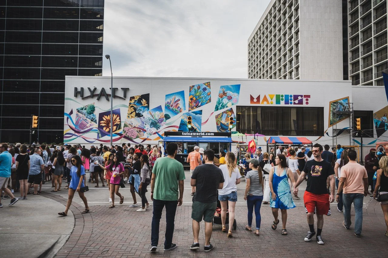 Crowd of people walking on city street in front of a building with colorful murals and the words 'Hyatt' and 'Maps' on it.