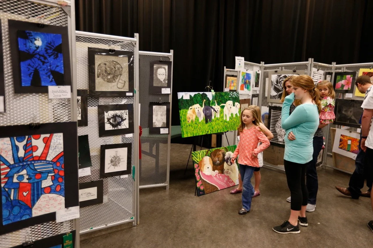 People viewing artwork at an art exhibition, with paintings displayed on metal panels.