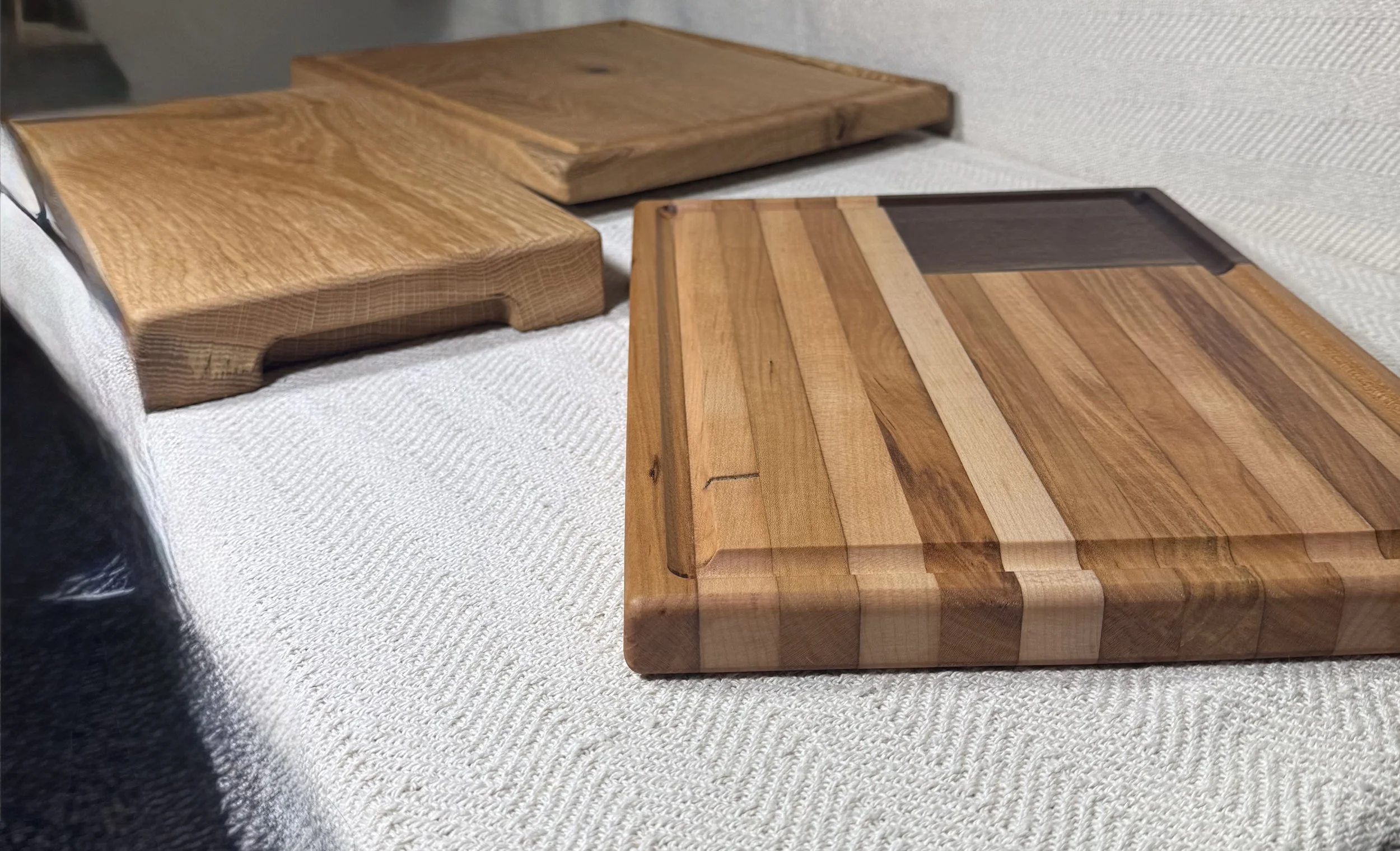 Three wooden cutting boards on a beige textured surface, with two being rectangular and one irregular shape.