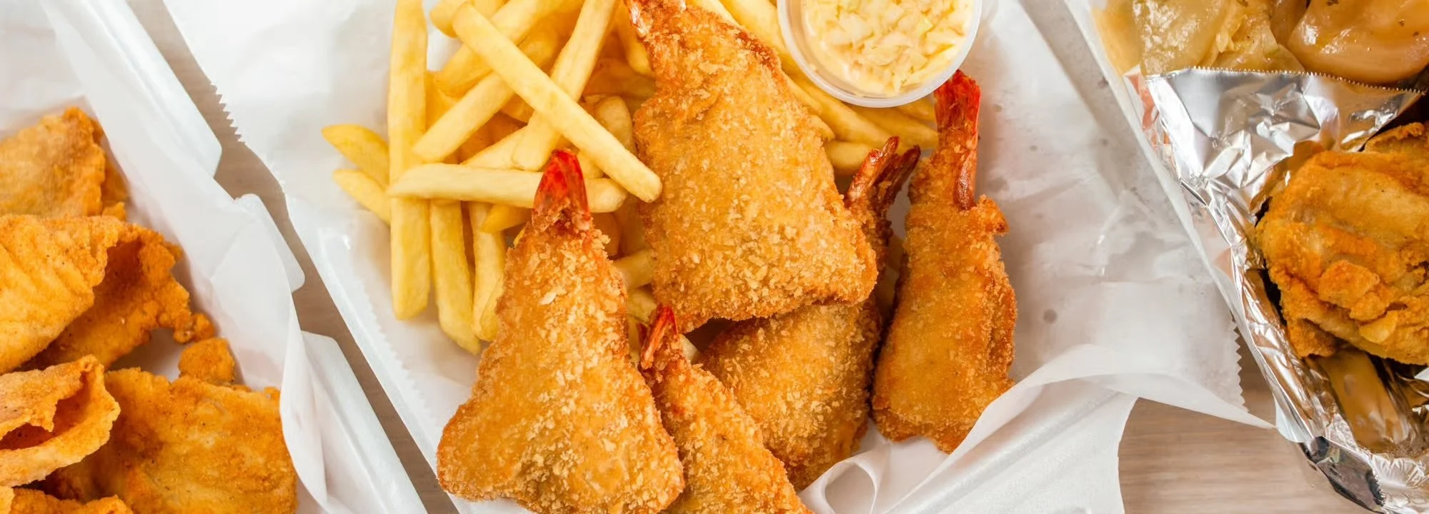 Fried shrimp with French fries and cole slaw on a takeout tray.