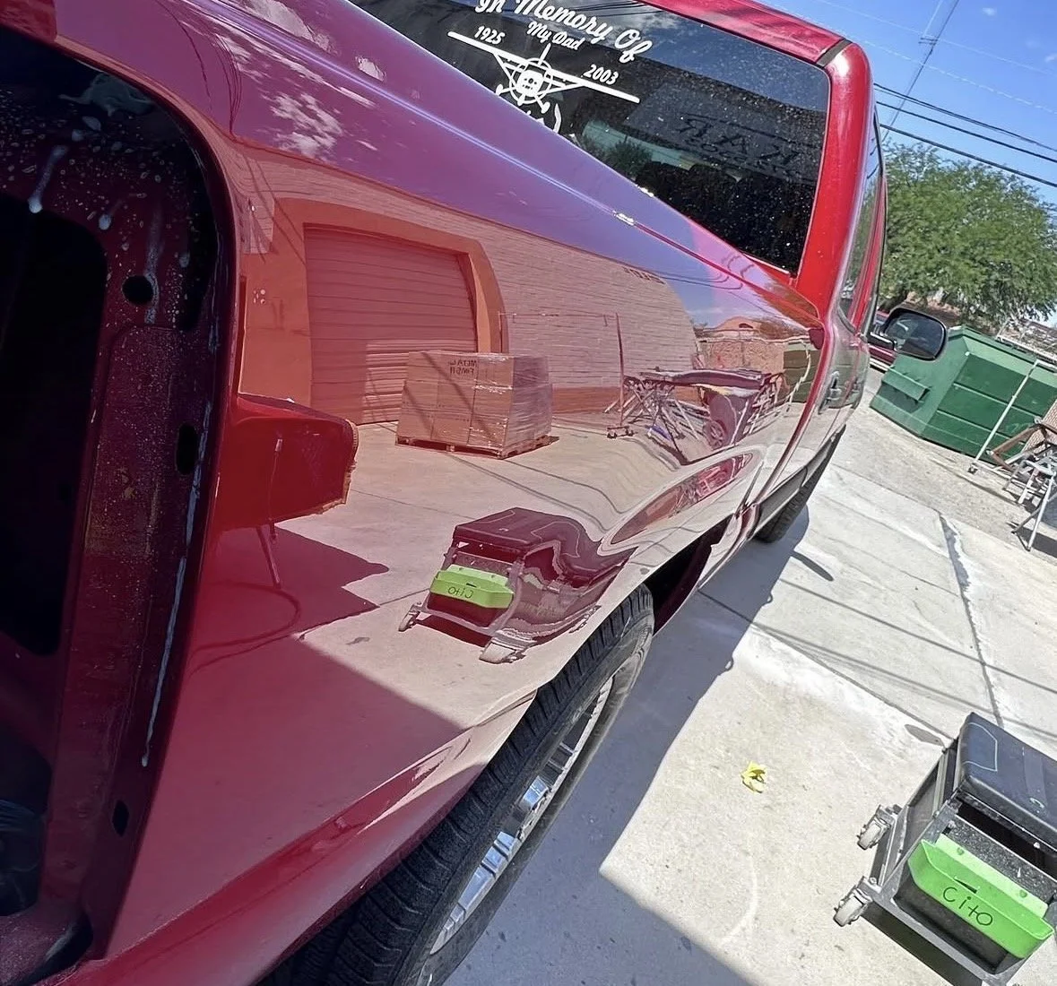Reflection of a red pickup truck in a garage door, with cardboard boxes, a folding chair, and a small green tool chest visible in the background.