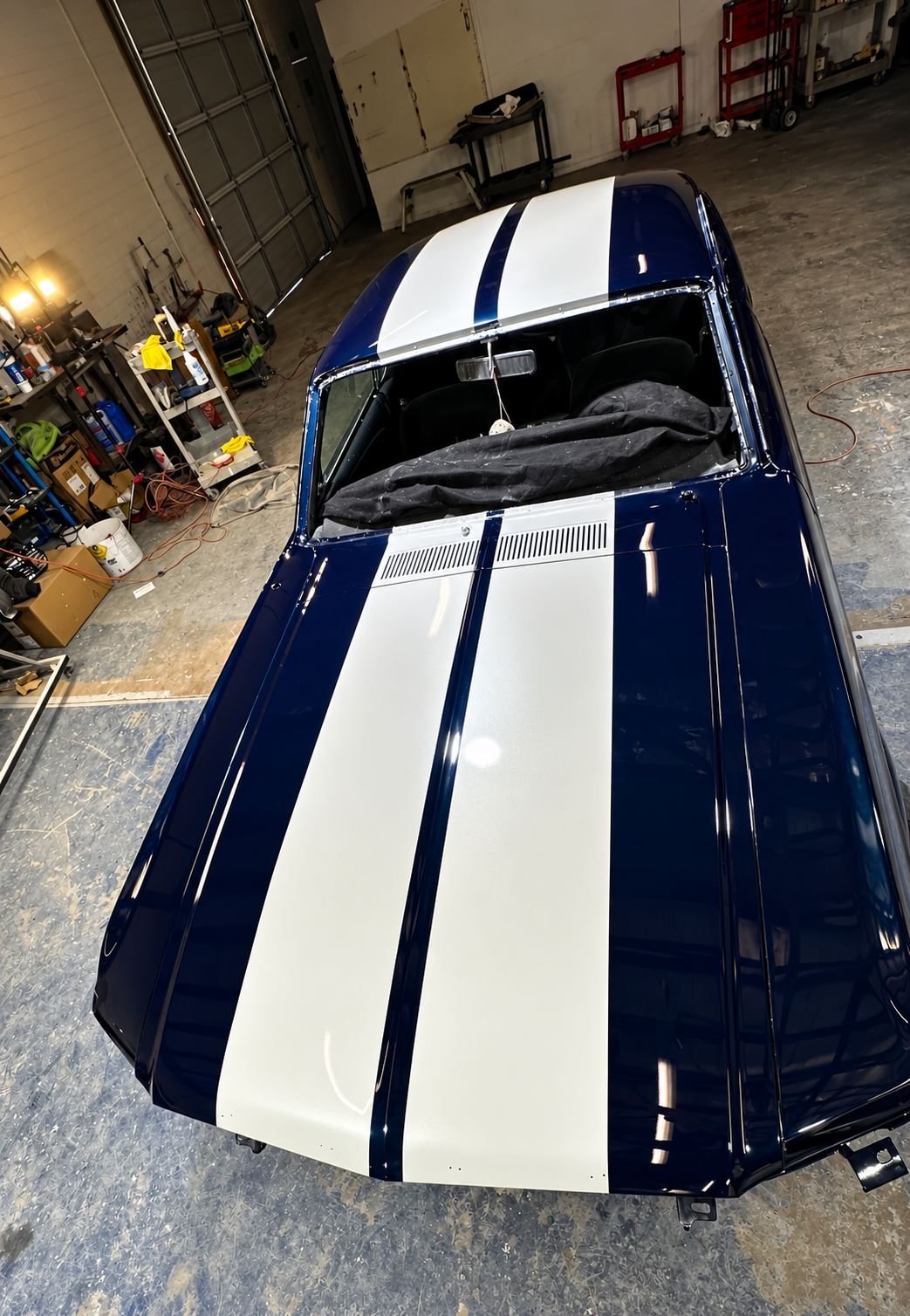 A vintage blue car with white racing stripes in a garage.