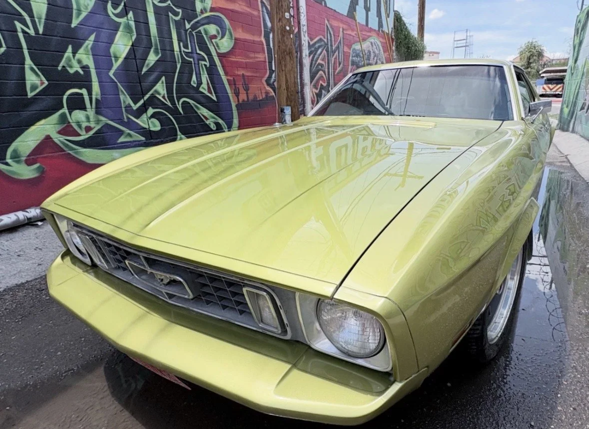 A vintage yellow Ford Mustang parked in front of a colorful graffiti wall.