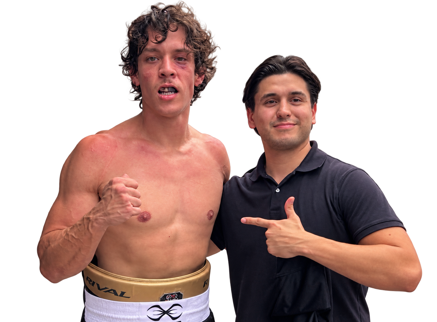 A shirtless man with curly hair and an injured eye, wearing boxing shorts, making a fist, next to a man in a black polo shirt pointing at him, both smiling, with a red and black background.